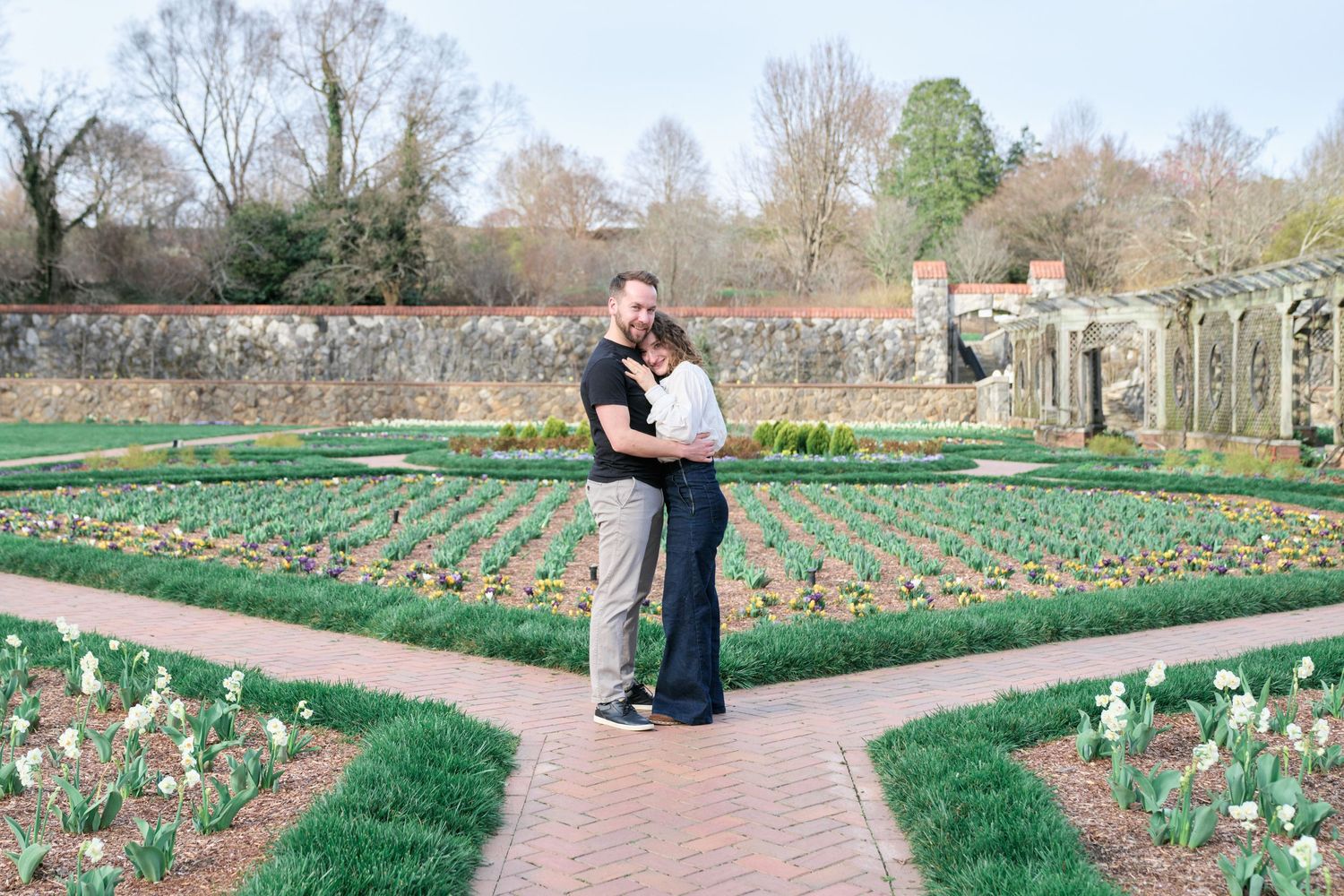 Couple hugging and smiling at the camera at the Biltmore gardens during their engagement photos.