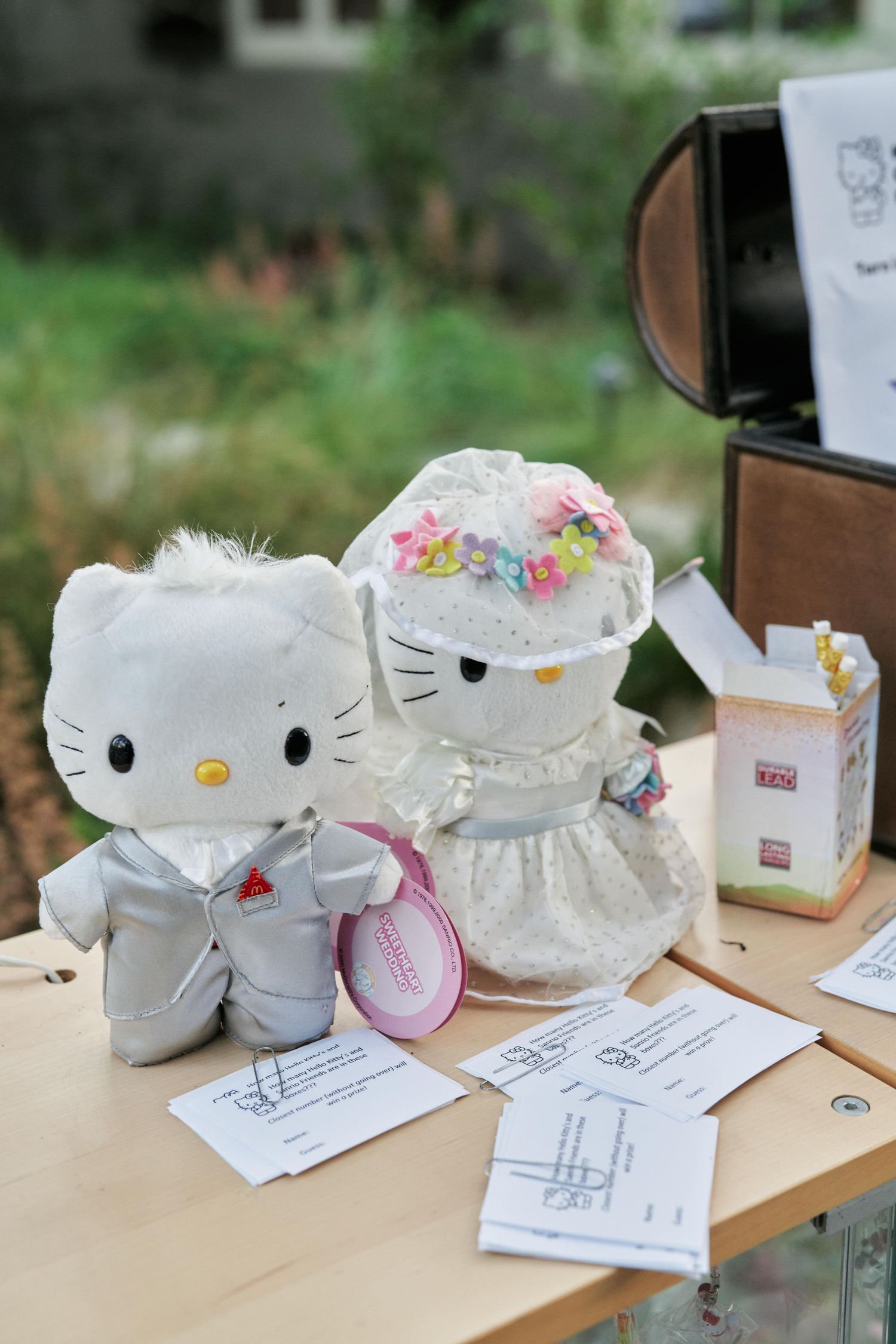 Hello Kitty bride and groom plush toys on display with wedding papers on wooden table.