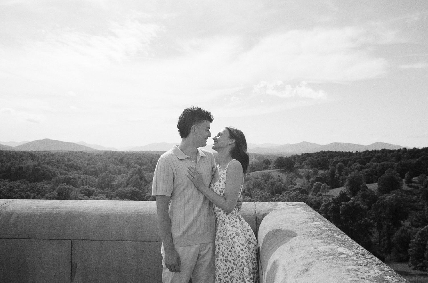 Black and white photo of a romantic couple sharing an intimate moment on a rooftop with scenic mountain views.