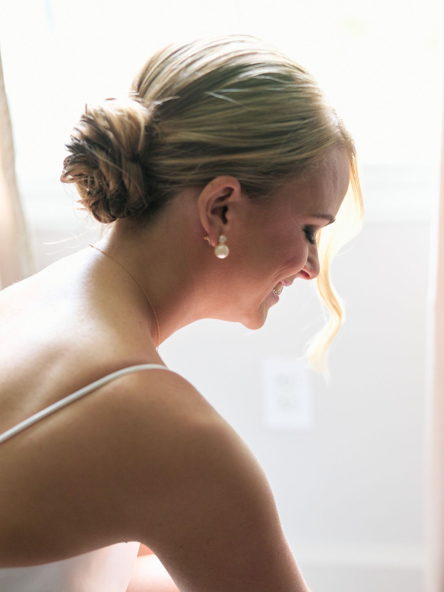 Side profile of a smiling person with an elegant updo hairstyle and pearl earring.