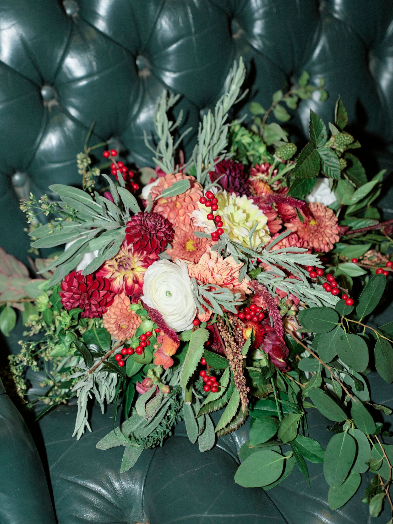 A lush floral arrangement with pink and red blooms against dark green tufted upholstery.