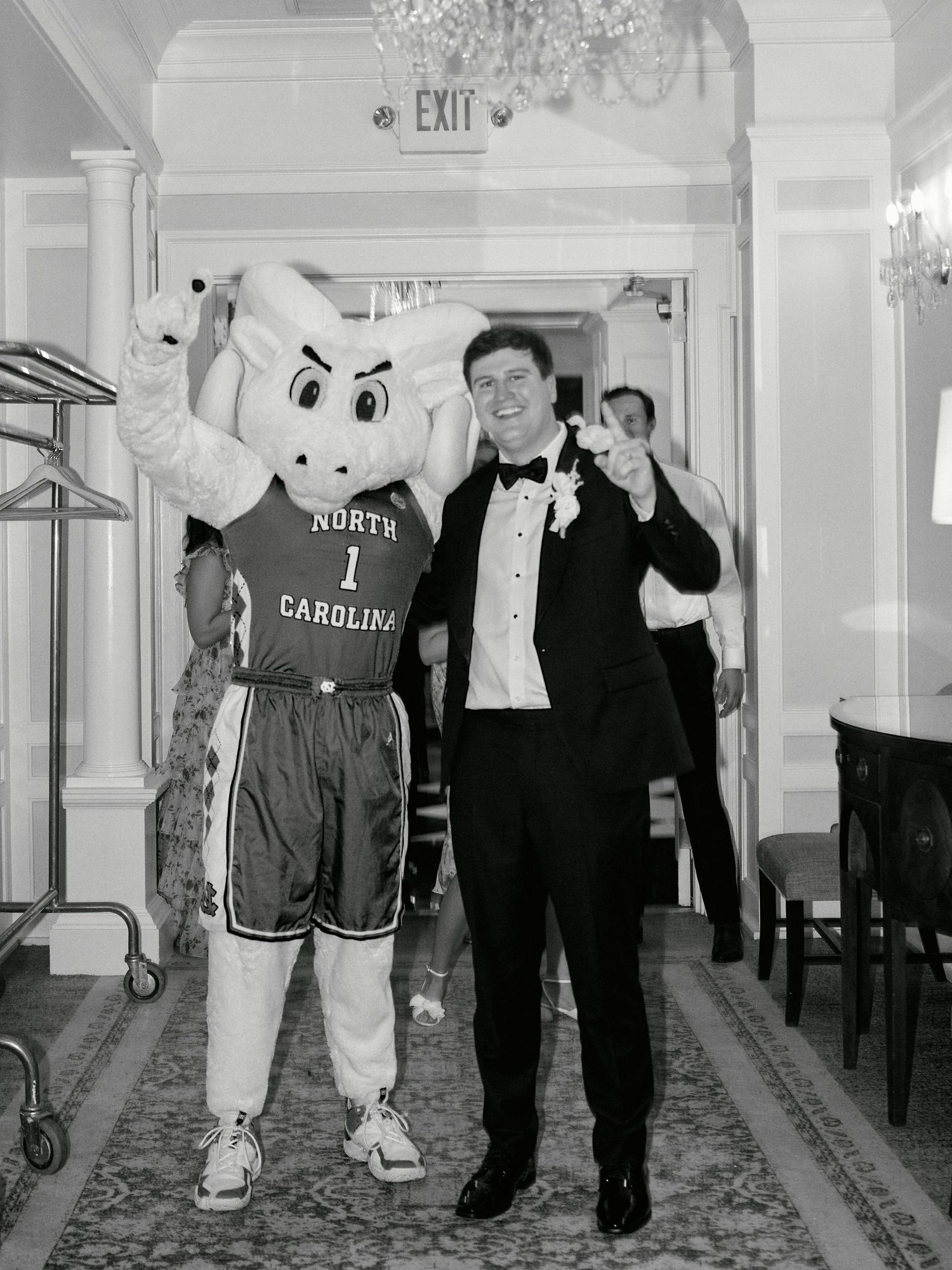 A person in formal attire poses with the North Carolina Tar Heels mascot at an event.