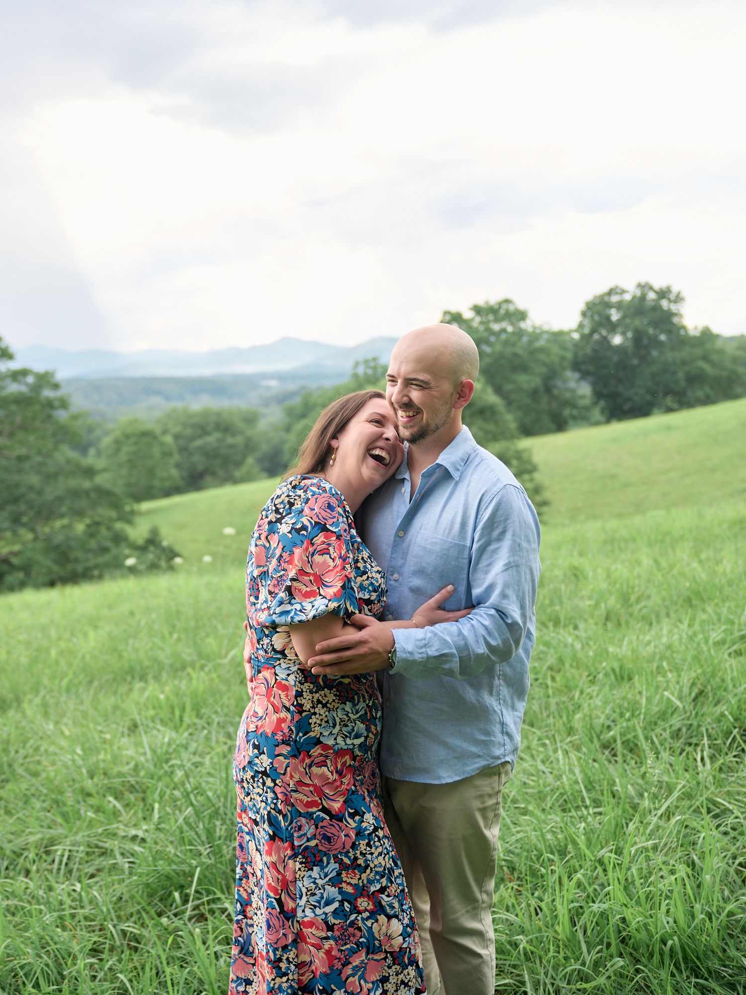 A couple shares a joyful moment together while standing in a lush green hillside meadow on a summer day.