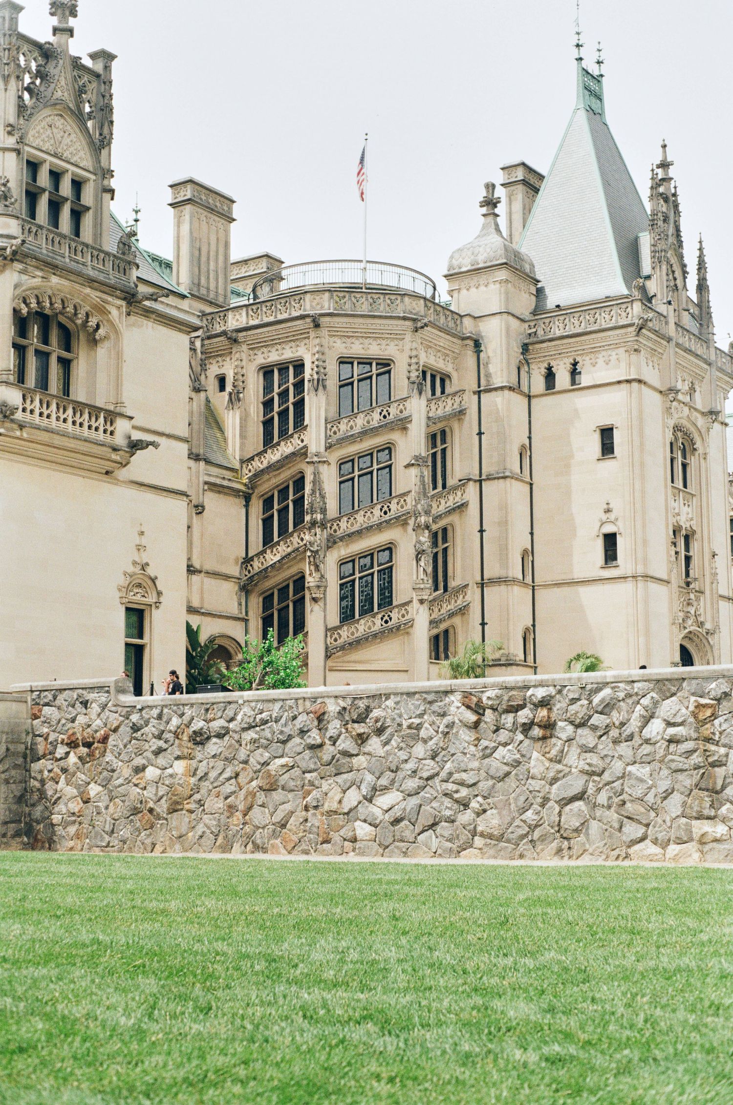 A majestic stone castle with Gothic architecture features ornate windows and a turret under cloudy skies.