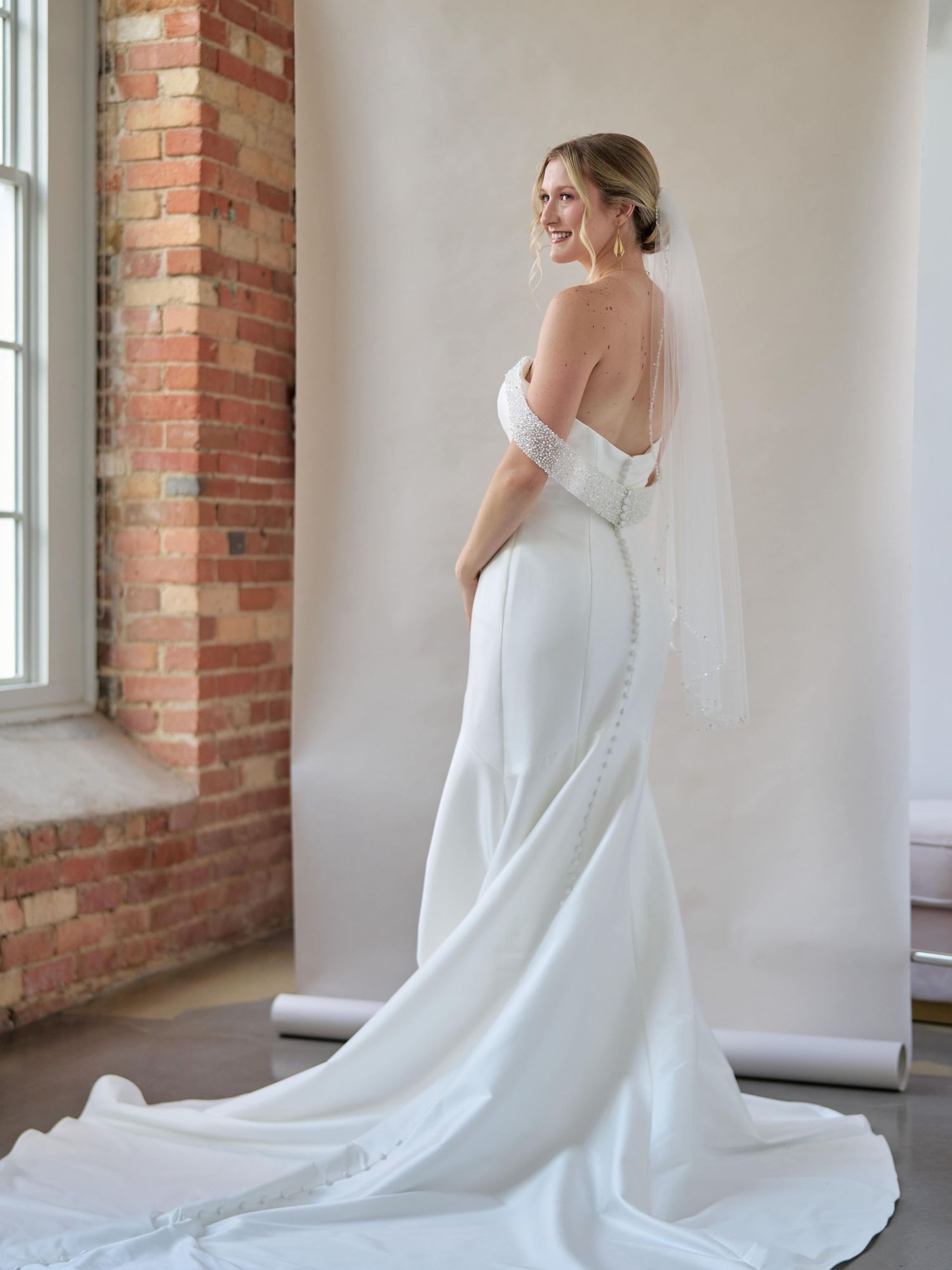 Elegant white wedding gown with sweetheart neckline and chapel train in brick-walled venue.