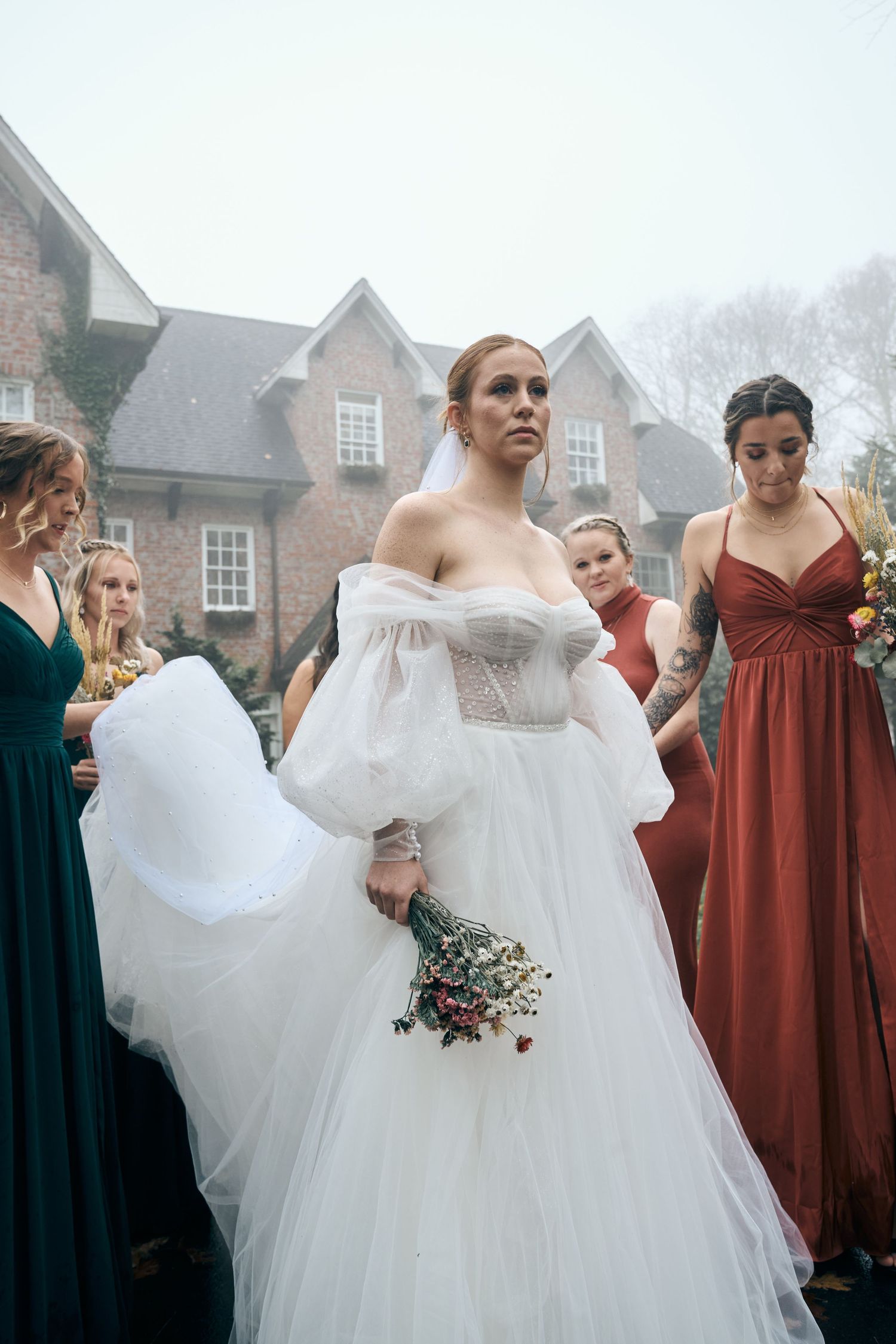 Wedding party gathered outdoors with bride in white gown and bridesmaids in jewel-toned dresses.