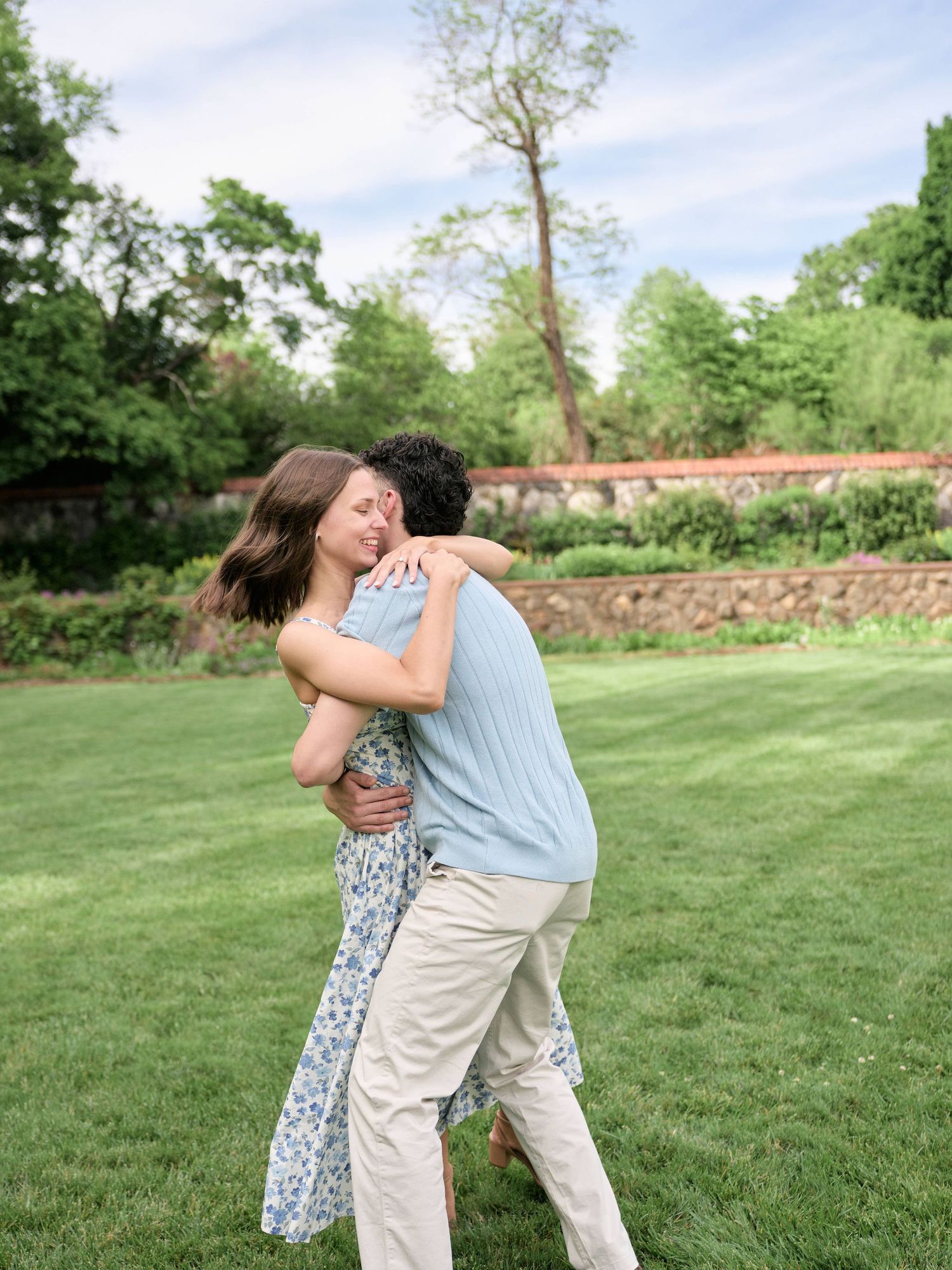 Couple embracing and spinning joyfully on a lush green lawn in a beautiful garden setting.