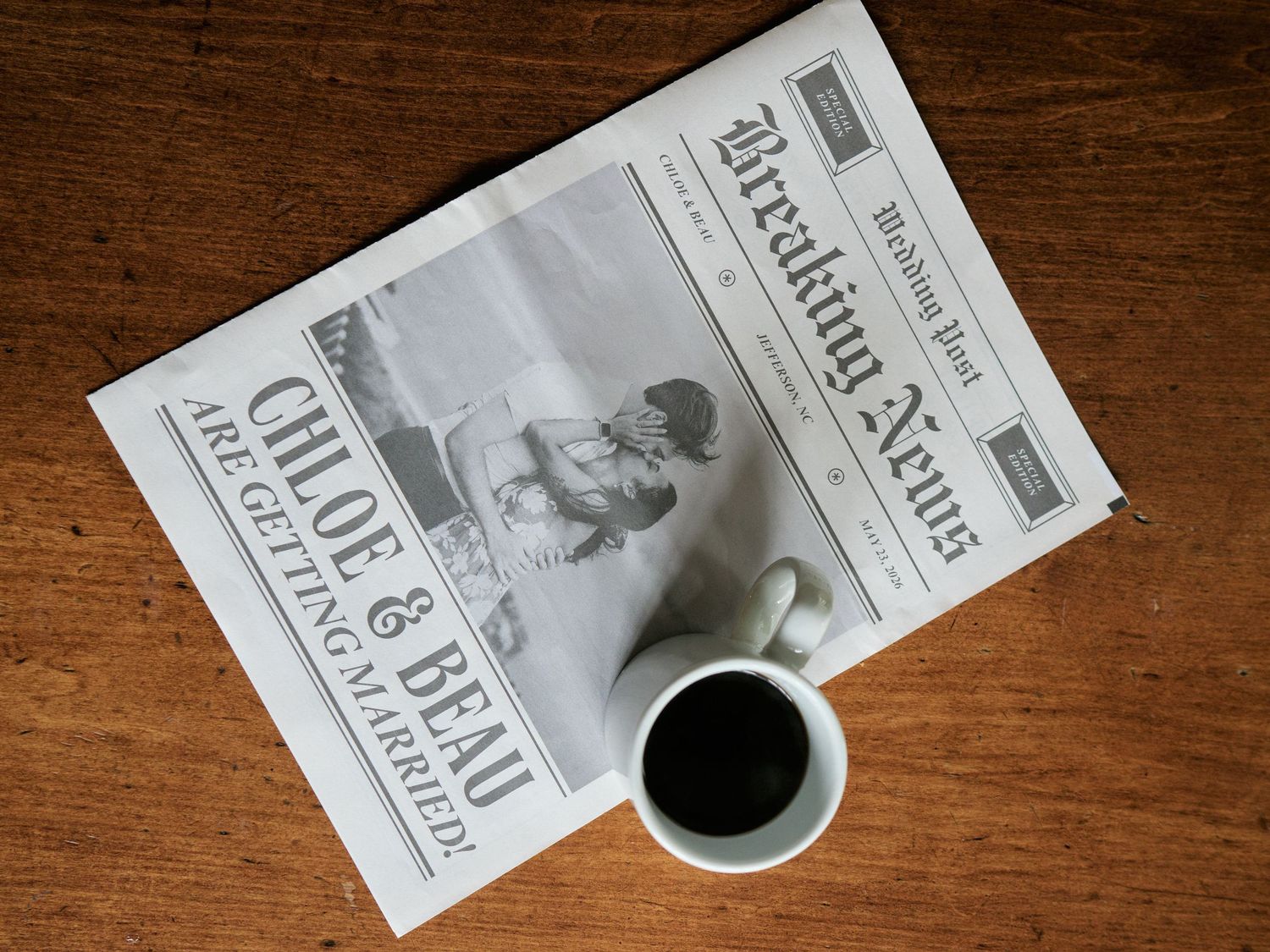 A personalized Breaking News wedding announcement newspaper beside a black coffee mug on a wooden table.