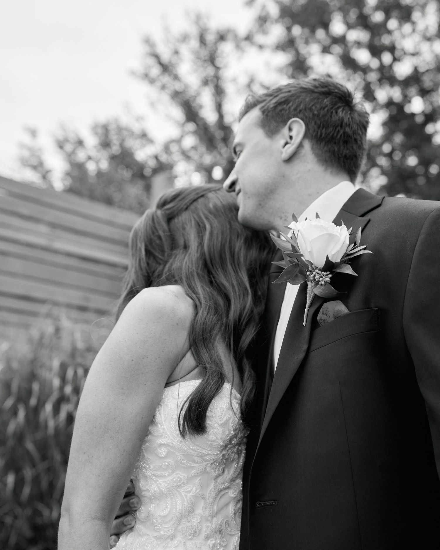 Black and white photo of a bride and groom sharing a kiss outdoors on their wedding day.