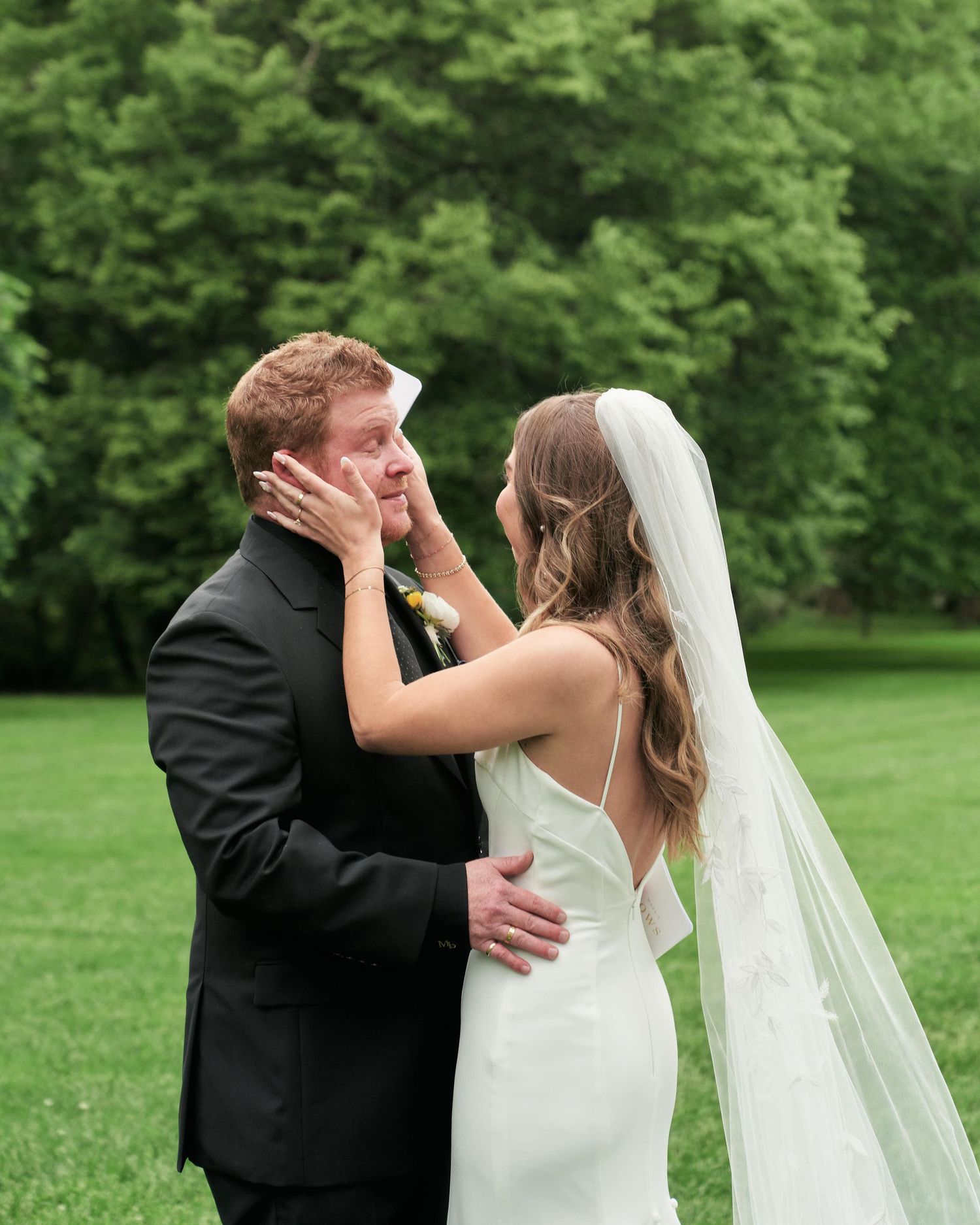 A couple shares a romantic kiss in a lush green garden setting while wearing formal wedding attire.