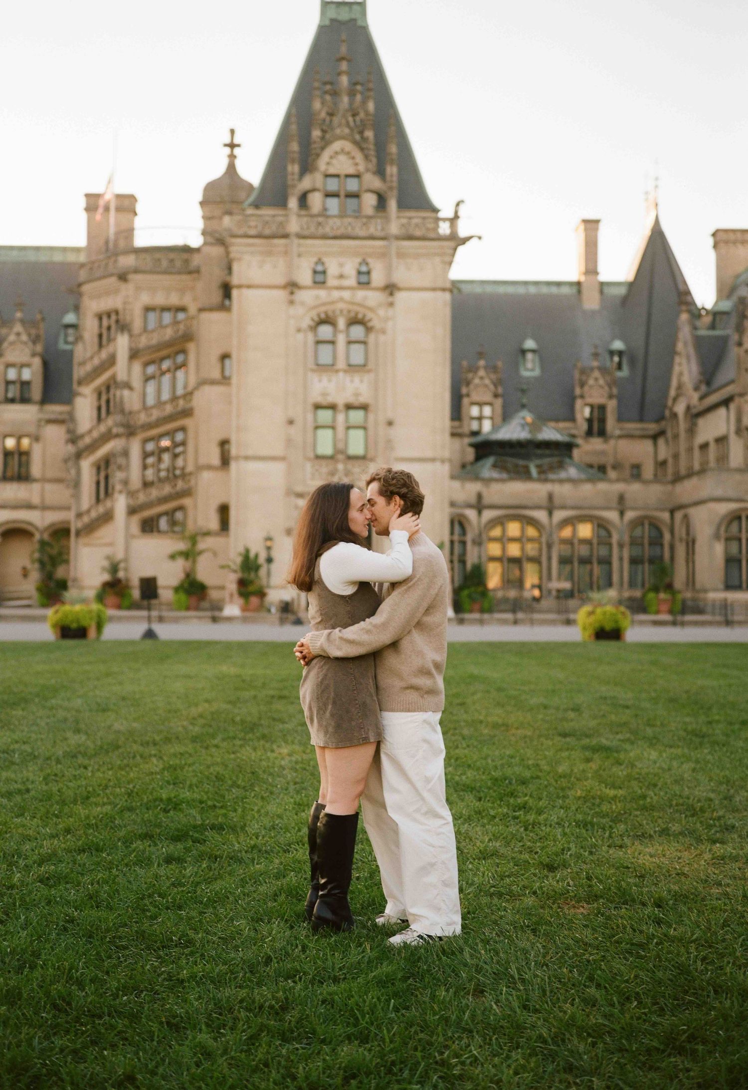 A couple shares a romantic kiss on the lawn in front of the grand Biltmore Estate in Asheville, NC.
