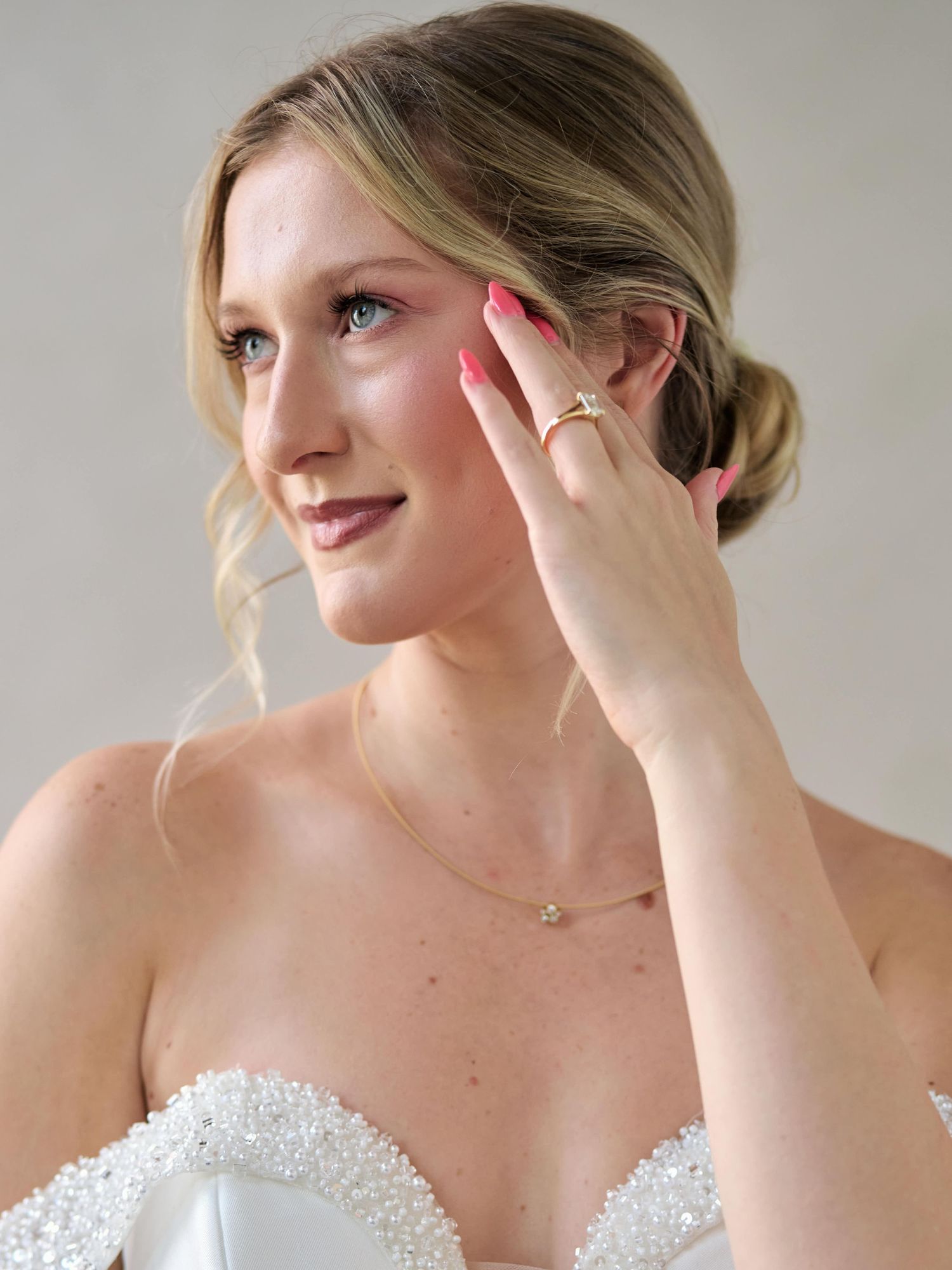 Portrait of bride in strapless beaded dress showing coral nails and elegant updo.