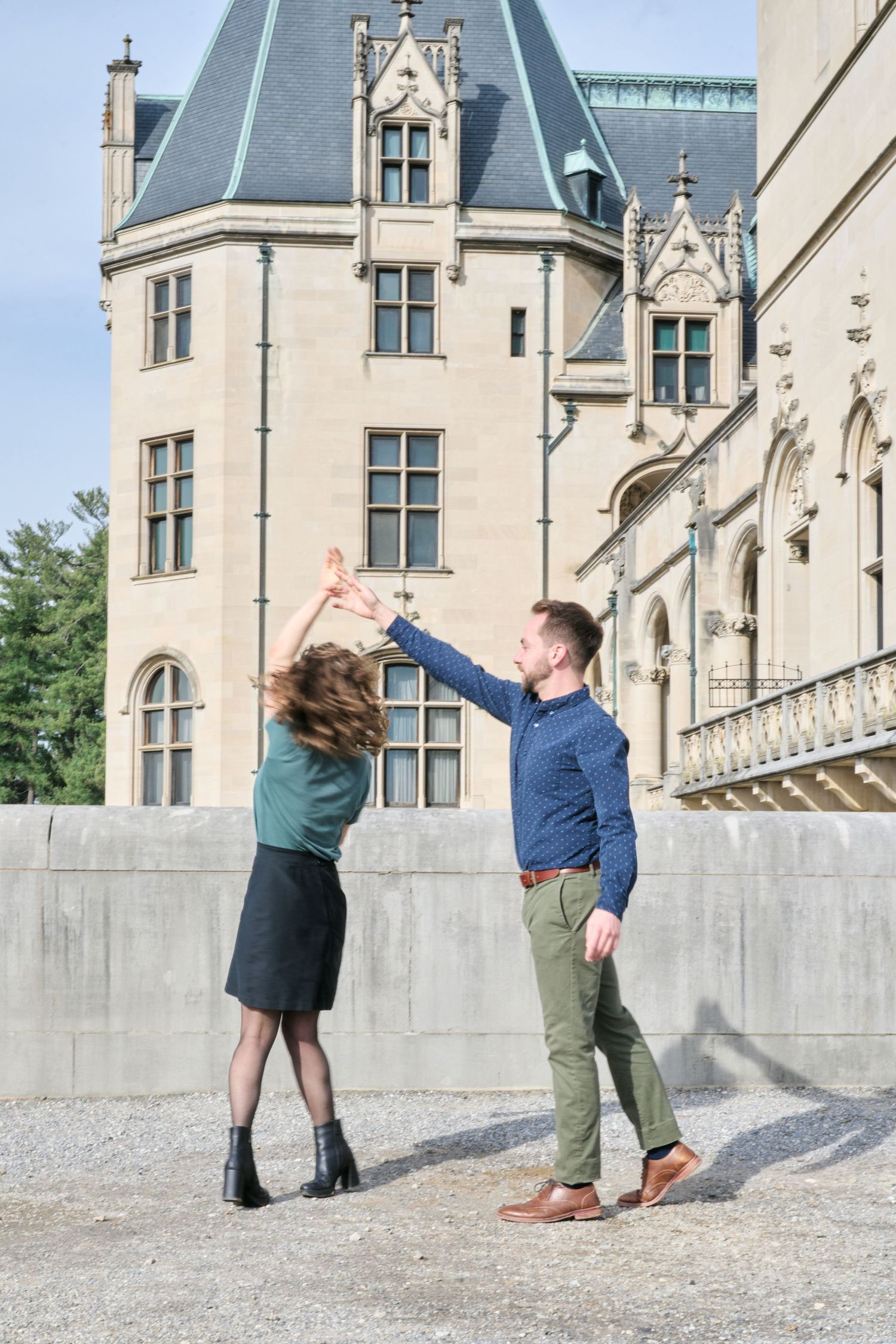 A couple dances playfully outside a grand Gothic-style mansion with ornate architecture.
