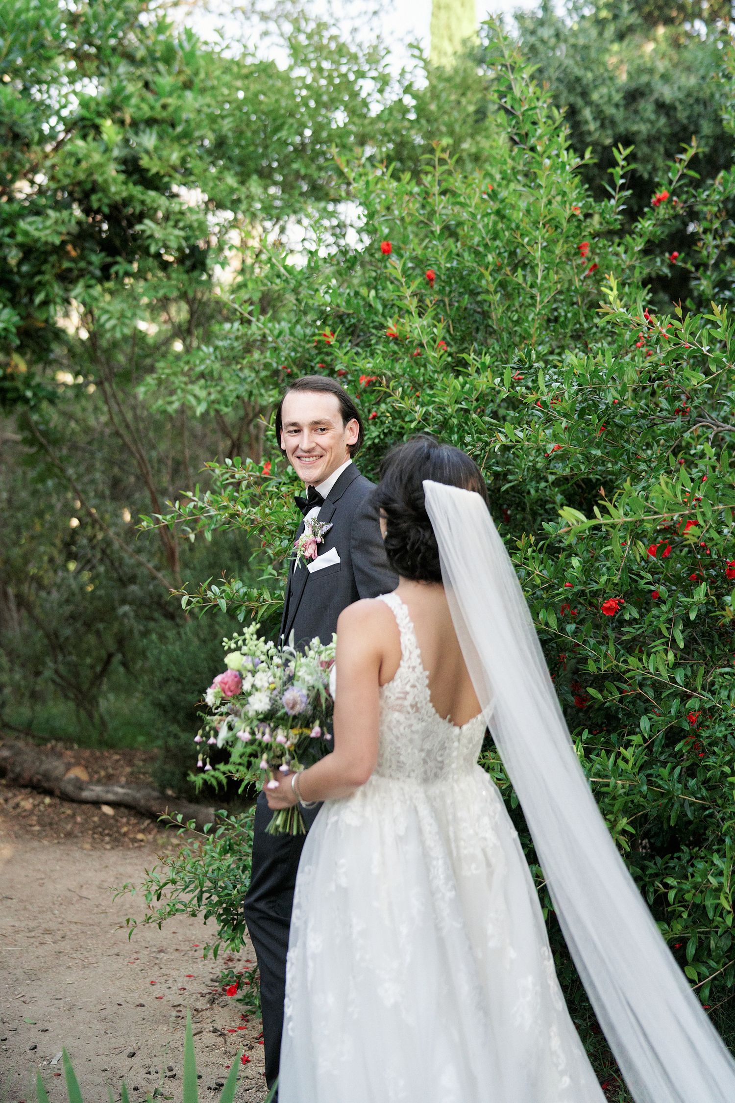 A joyful wedding couple sharing a moment in a garden setting with greenery.