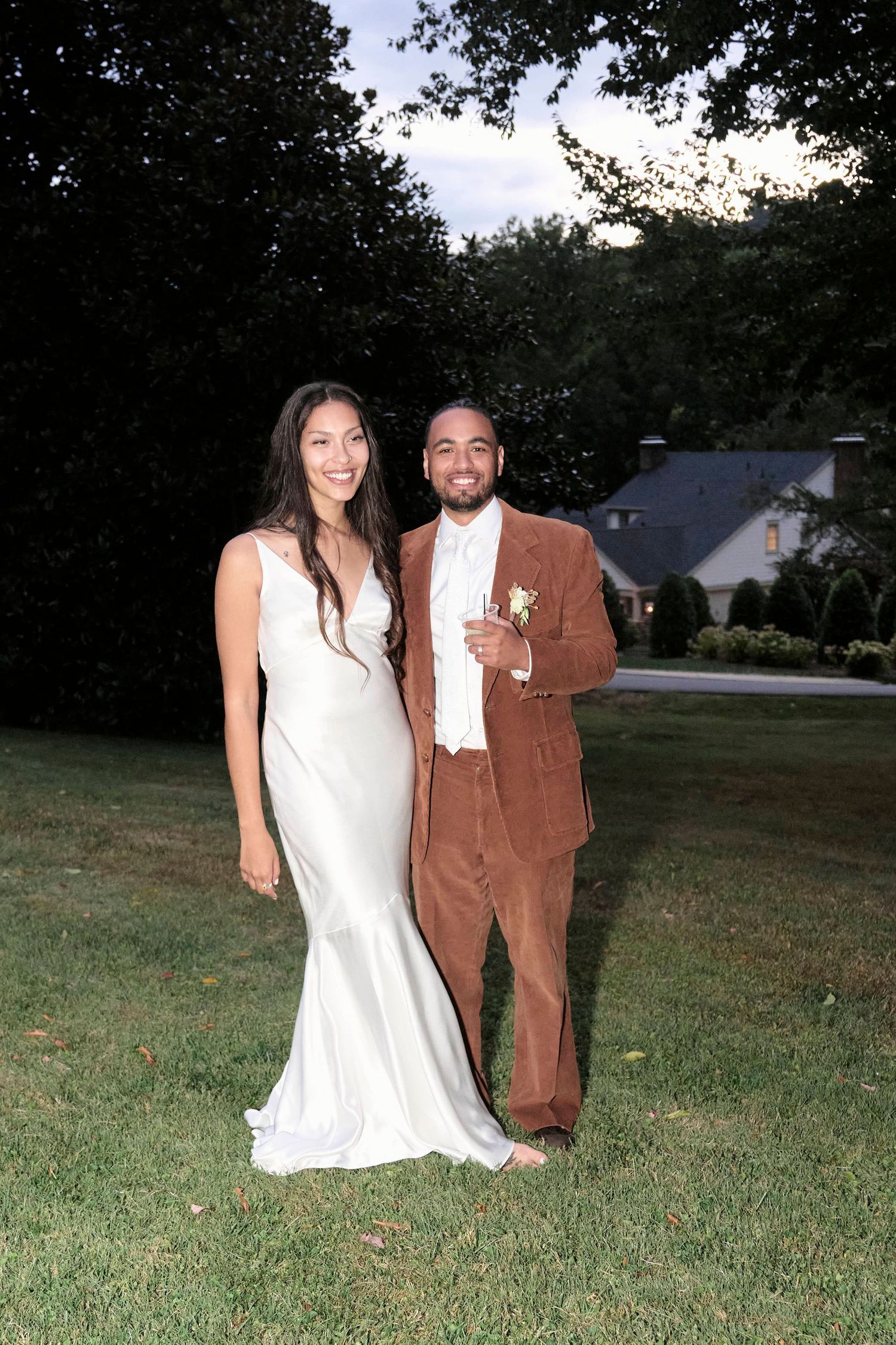 A couple poses on their wedding day, with the bride in white and groom in brown corduroy.