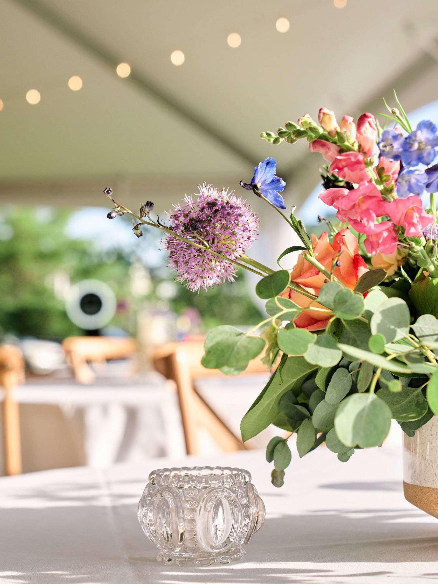 Elegant floral centerpiece with string lights and crystal votive holder on white tablecloth.
