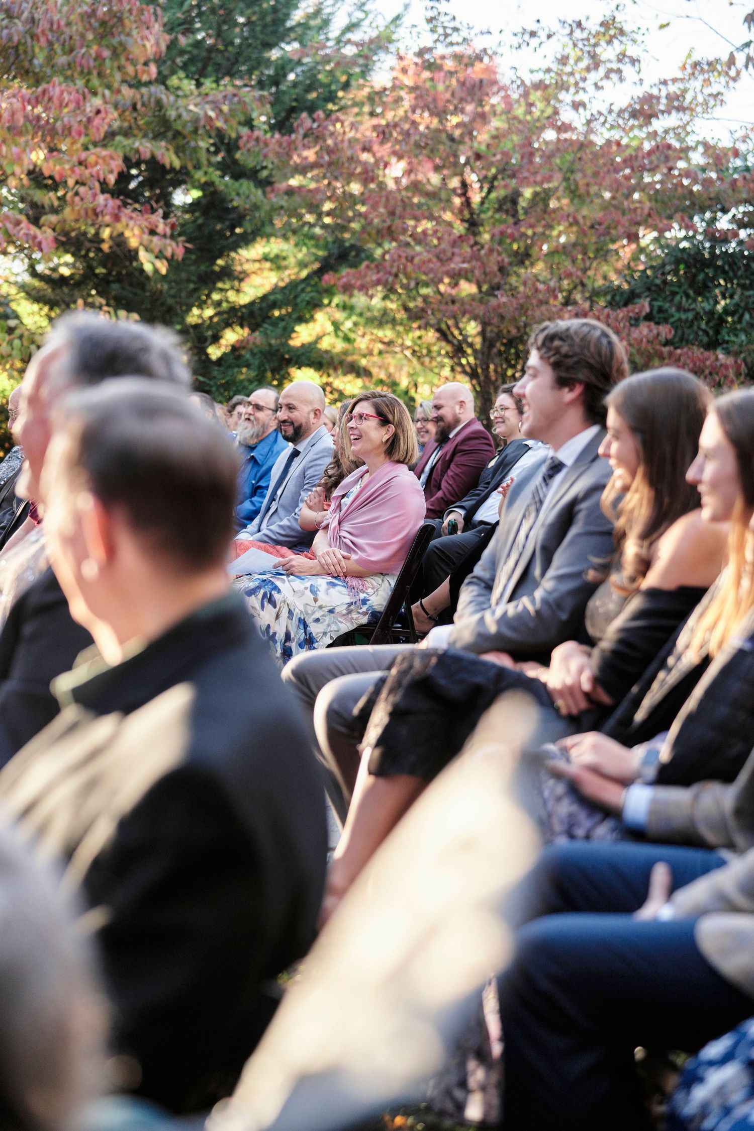 Wedding guests seated outdoors enjoying the ceremony among beautiful fall foliage.