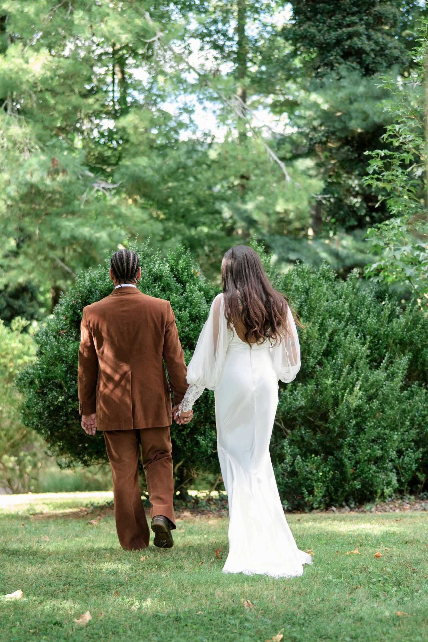 Bride and groom holding hands walking on a green field surrounded by greenery in Tennessee.