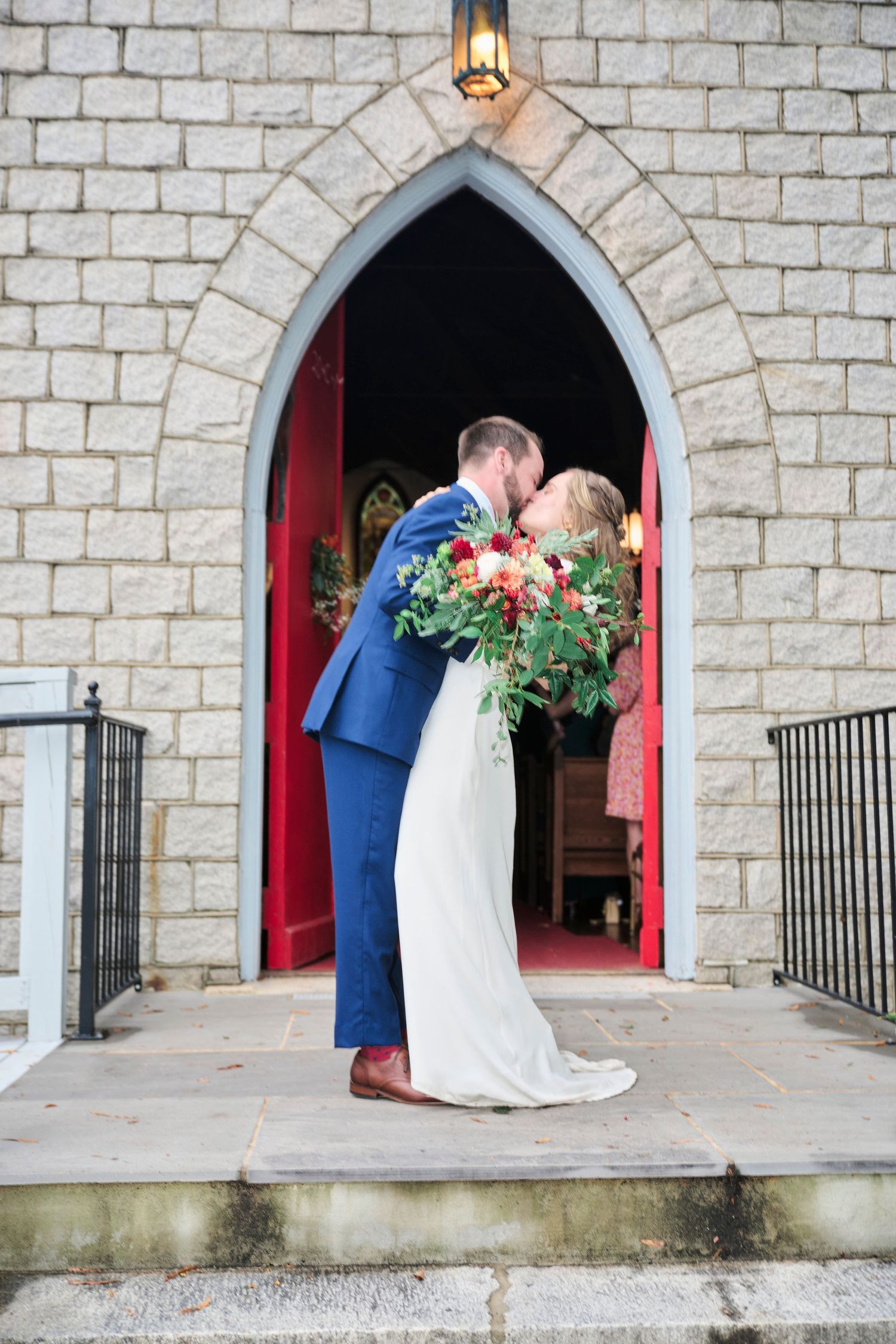 A tender moment shared outside a stone church entrance with Gothic arched doorway.