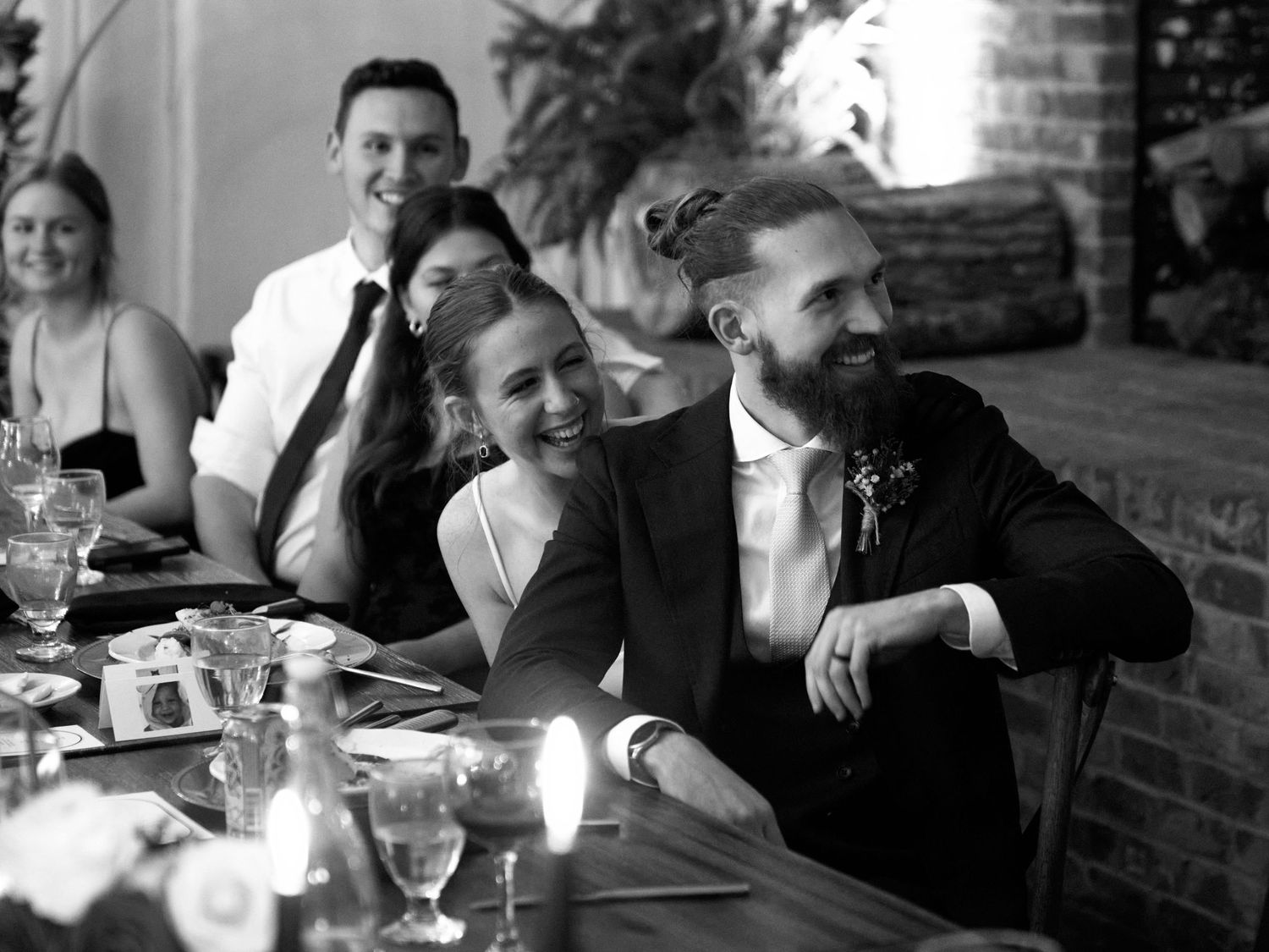 Black and white photo of wedding reception guests laughing together at dinner table.
