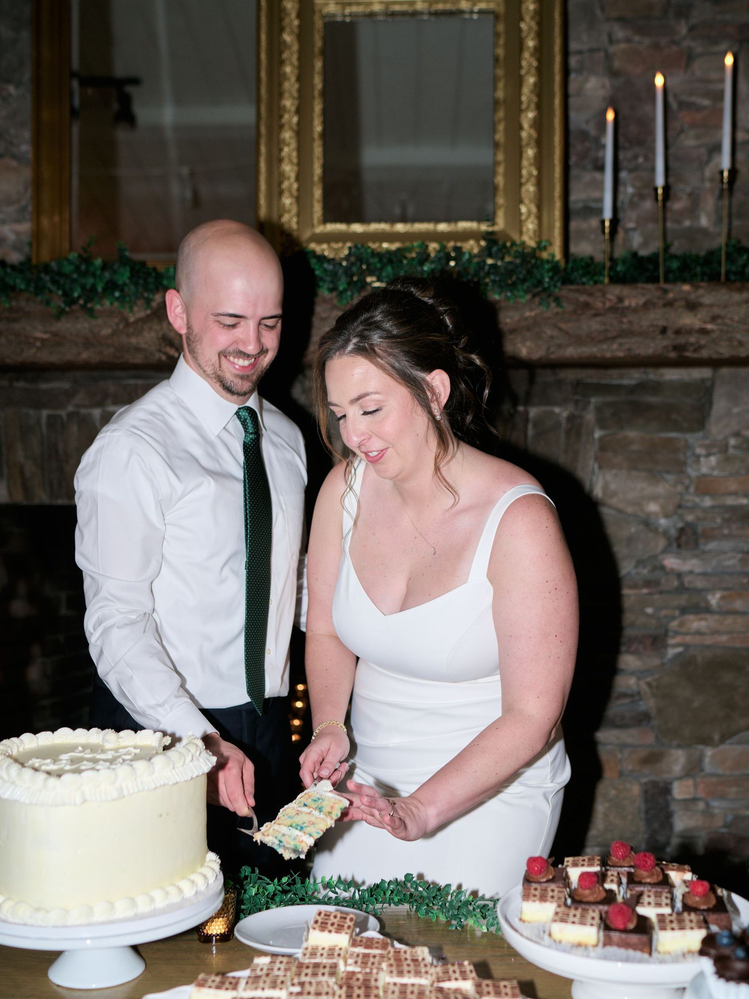 A couple cutting their wedding cake together at the dessert table with candles in the background.
