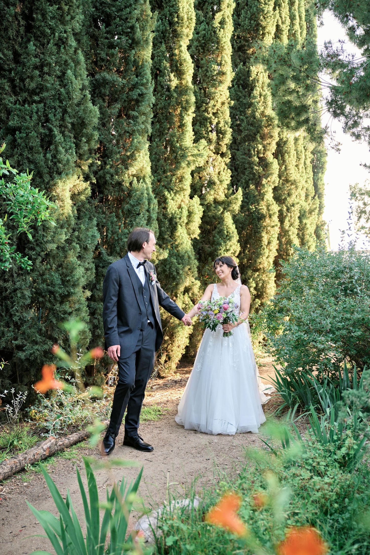 A couple shares a joyful moment on their wedding day surrounded by lush garden landscaping.