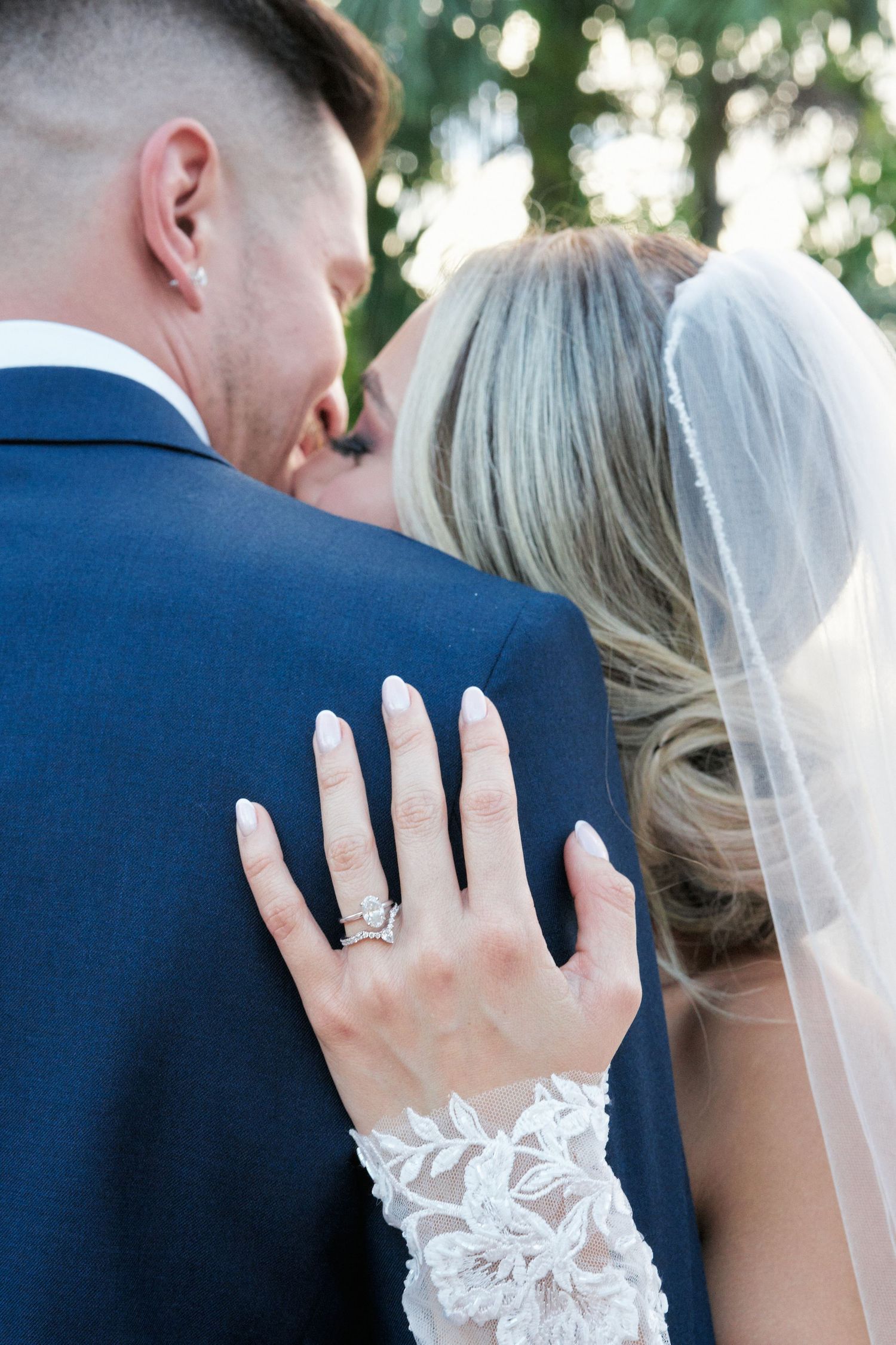 Close-up of bride's lace-detailed sleeve and engagement ring as she embraces groom.