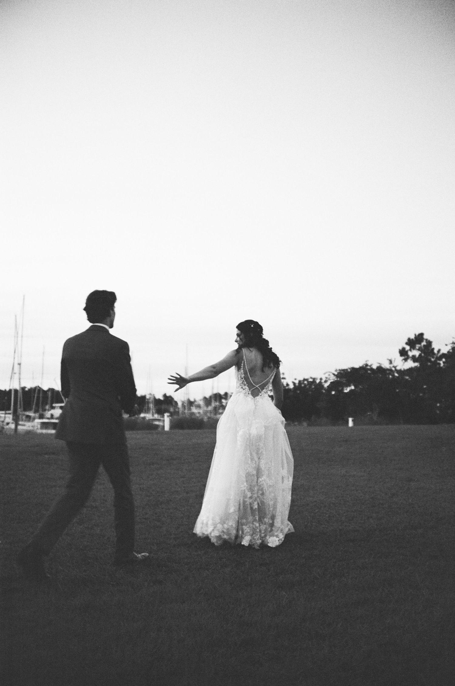 A black and white photo of a couple dancing at an outdoor wedding, with the bride wearing a flowing lace gown.