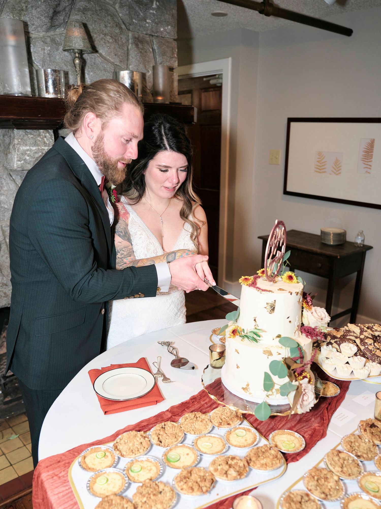 A couple cuts their wedding cake together at a rustic stone venue with dessert table.