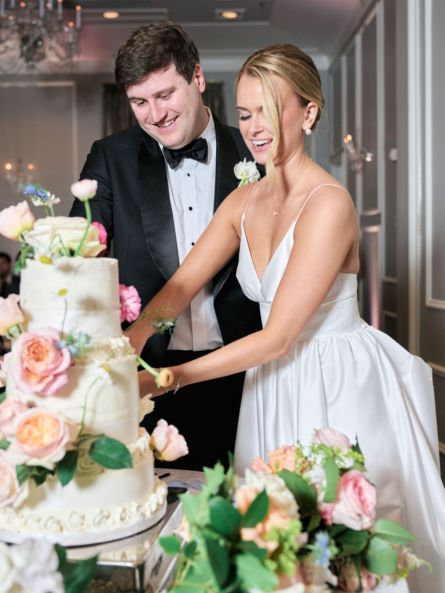 A couple cuts their elegant wedding cake decorated with pink and peach roses.