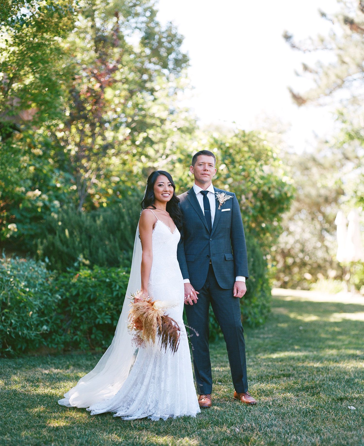 Elegant wedding portrait of couple in white dress and navy suit against natural garden backdrop.