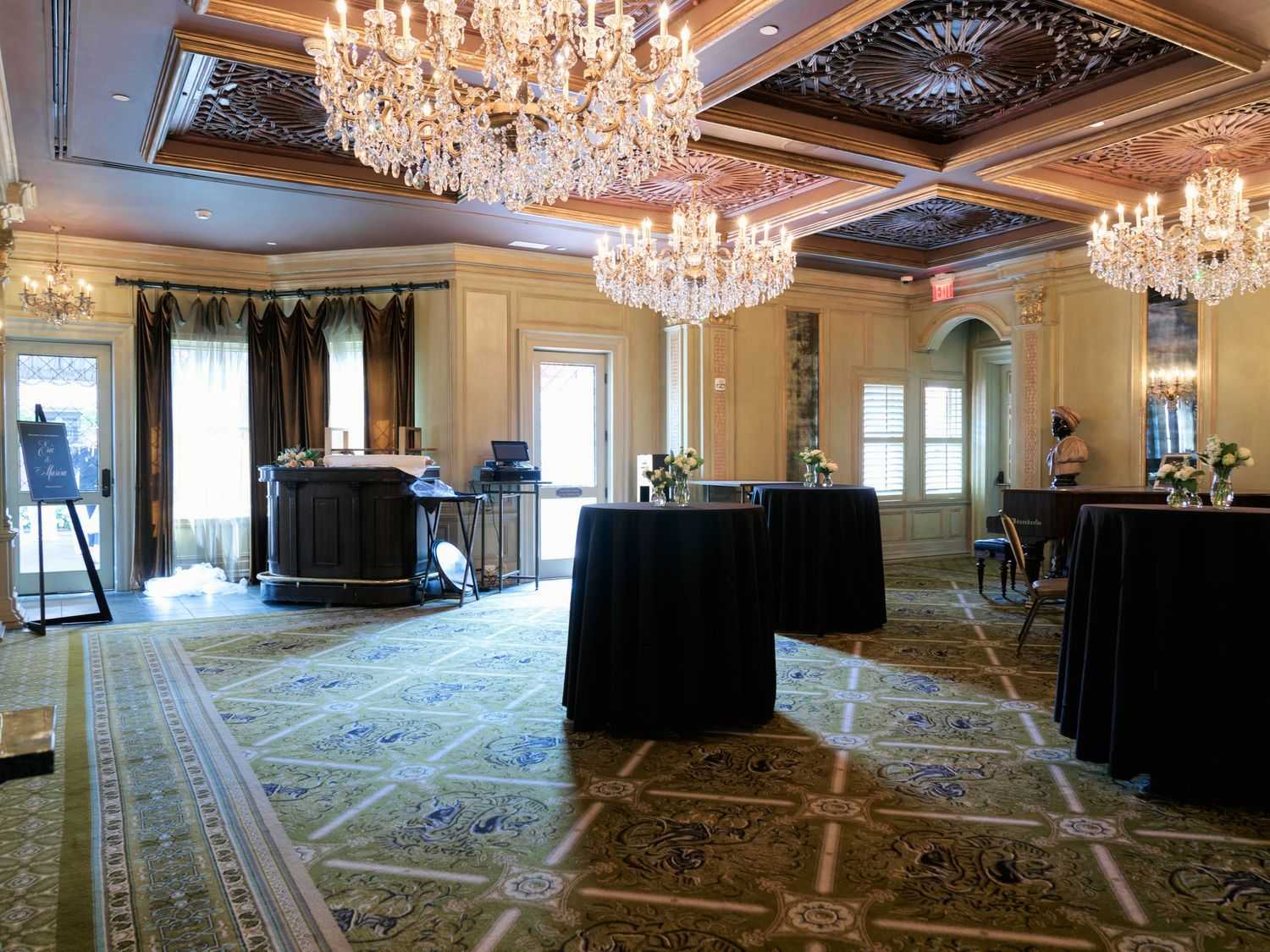 Elegant ballroom with crystal chandeliers and cocktail tables on ornate carpeted floor.