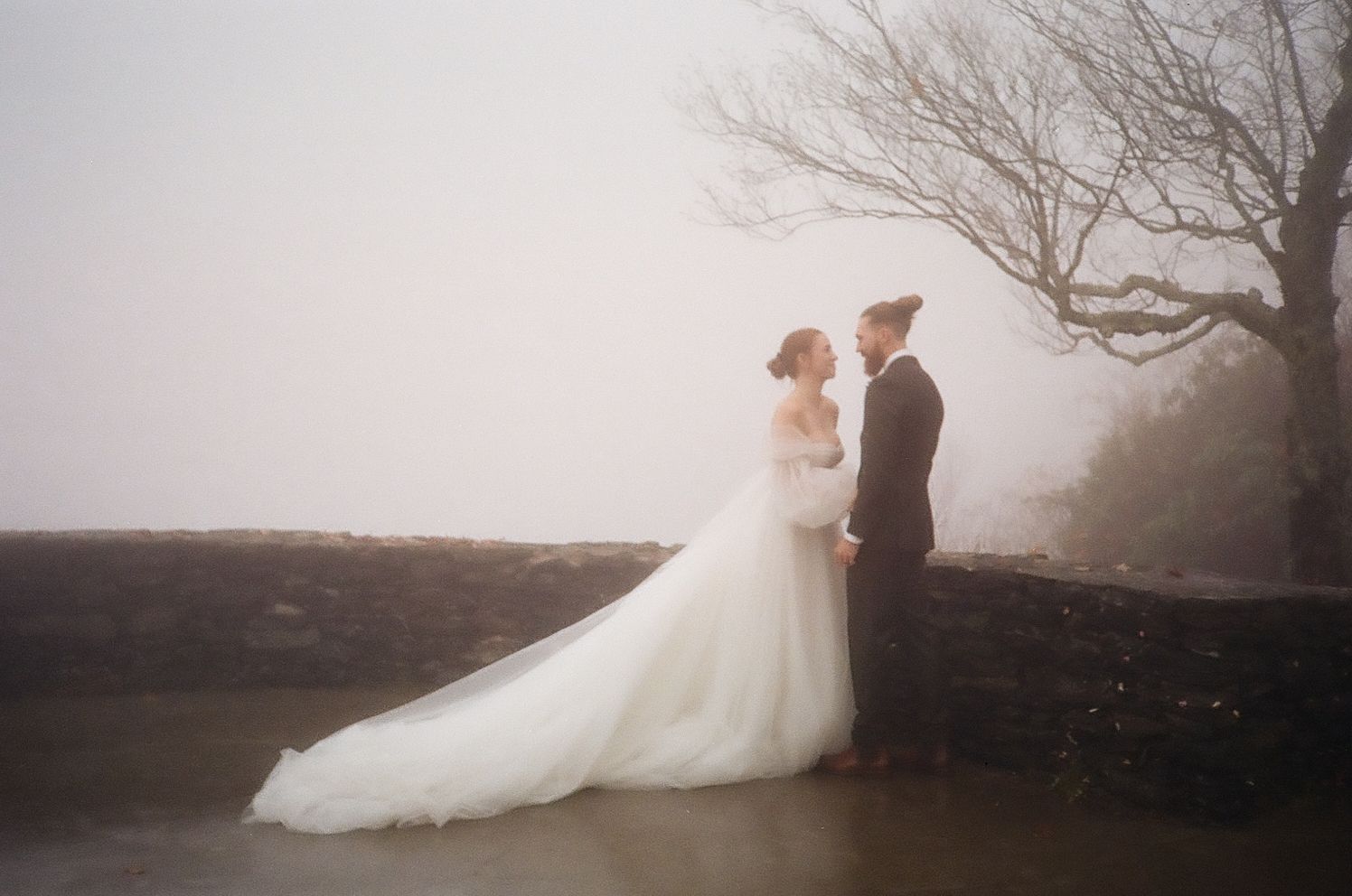Romantic wedding portrait of couple standing in misty outdoor setting with dramatic fog.