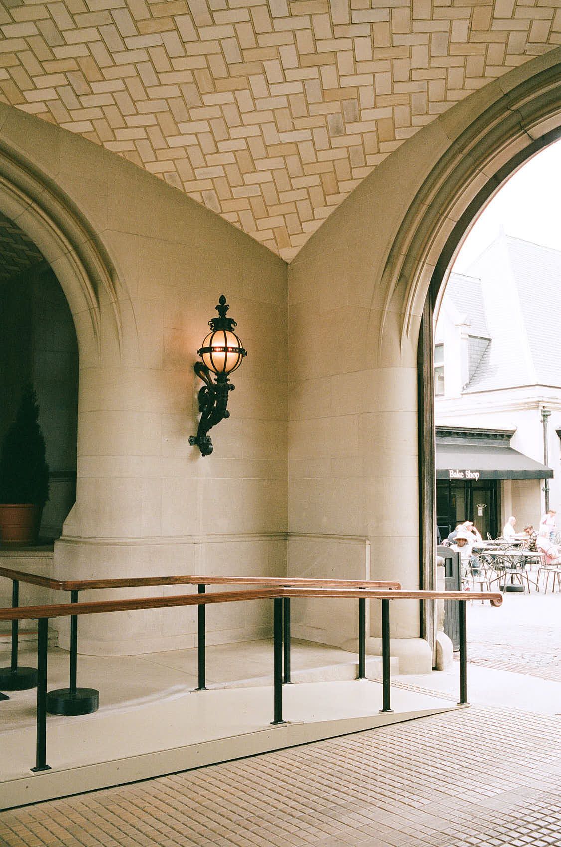 Elegant stone archway with ornate wall lantern and wooden railing in a classic architectural corridor.