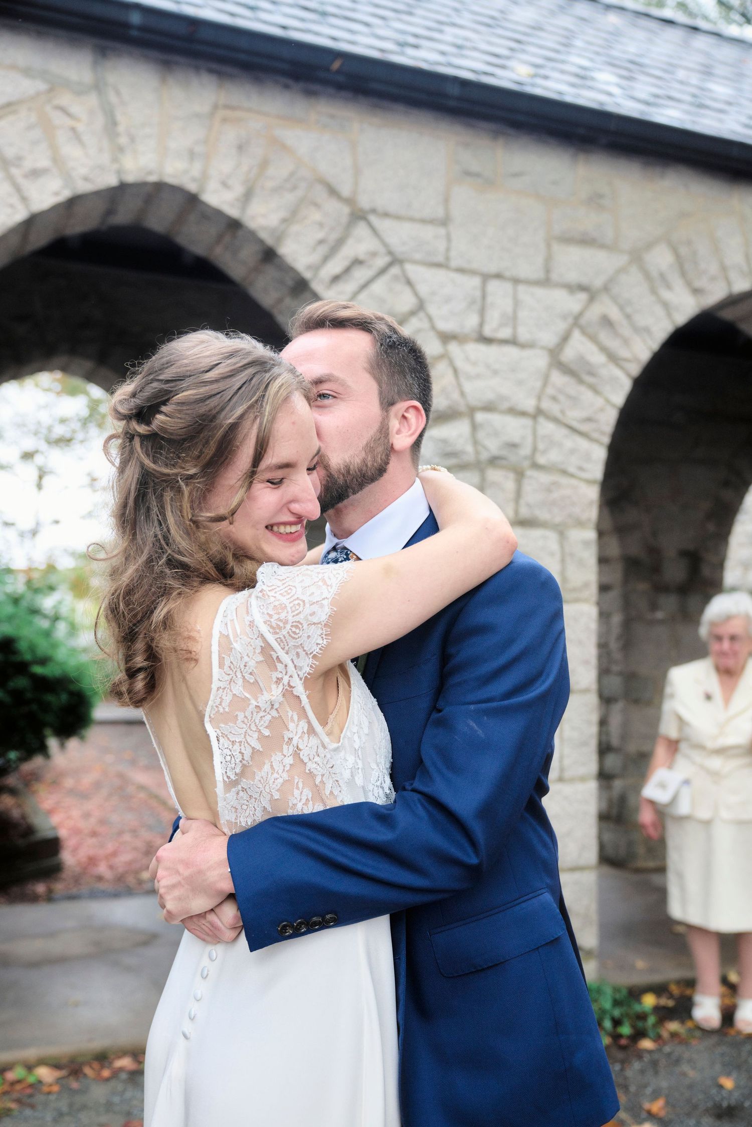A romantic wedding moment captured outside a stone church with arched walkways.