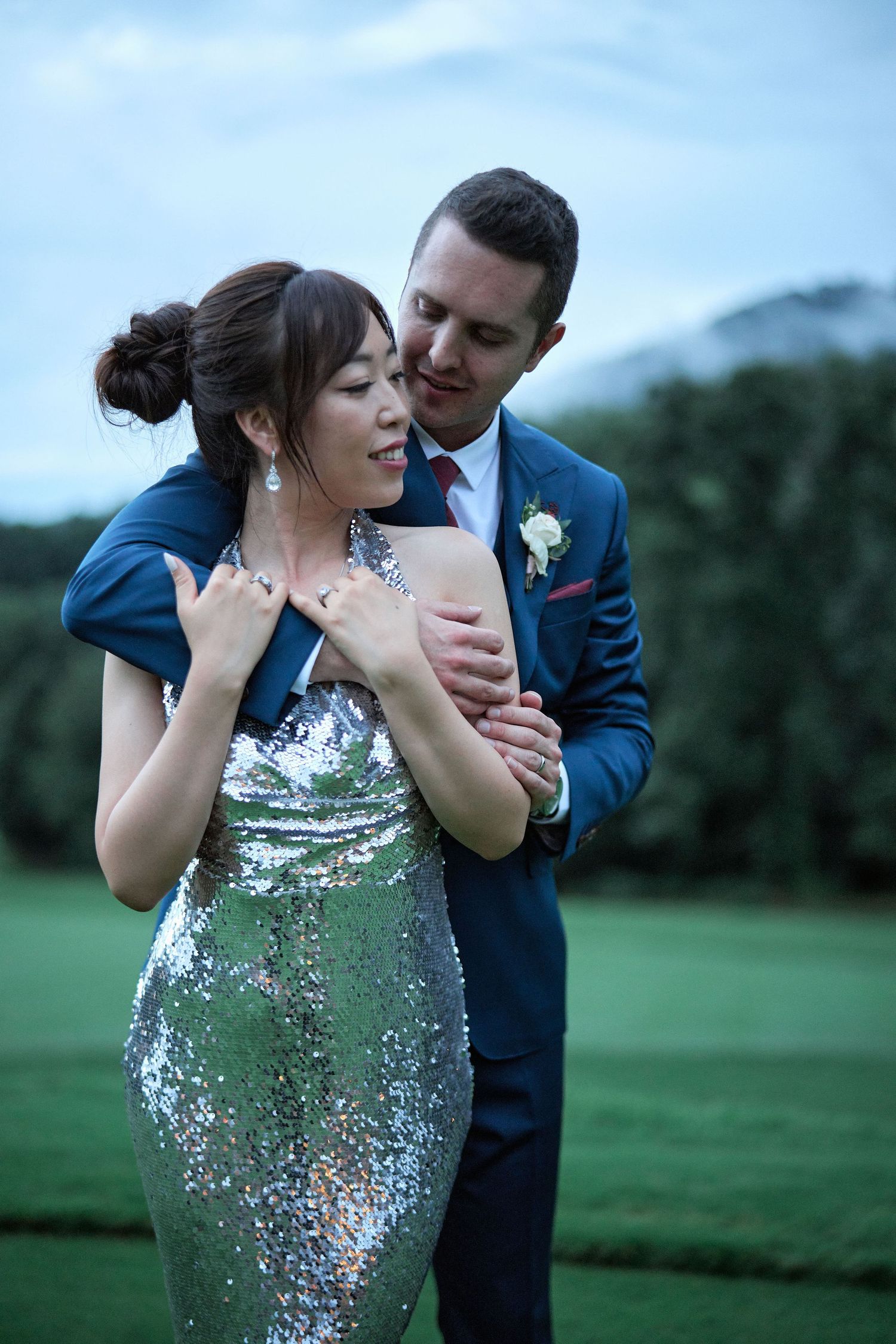 A tender moment between newlyweds on a golf course as the groom embraces his bride from behind.