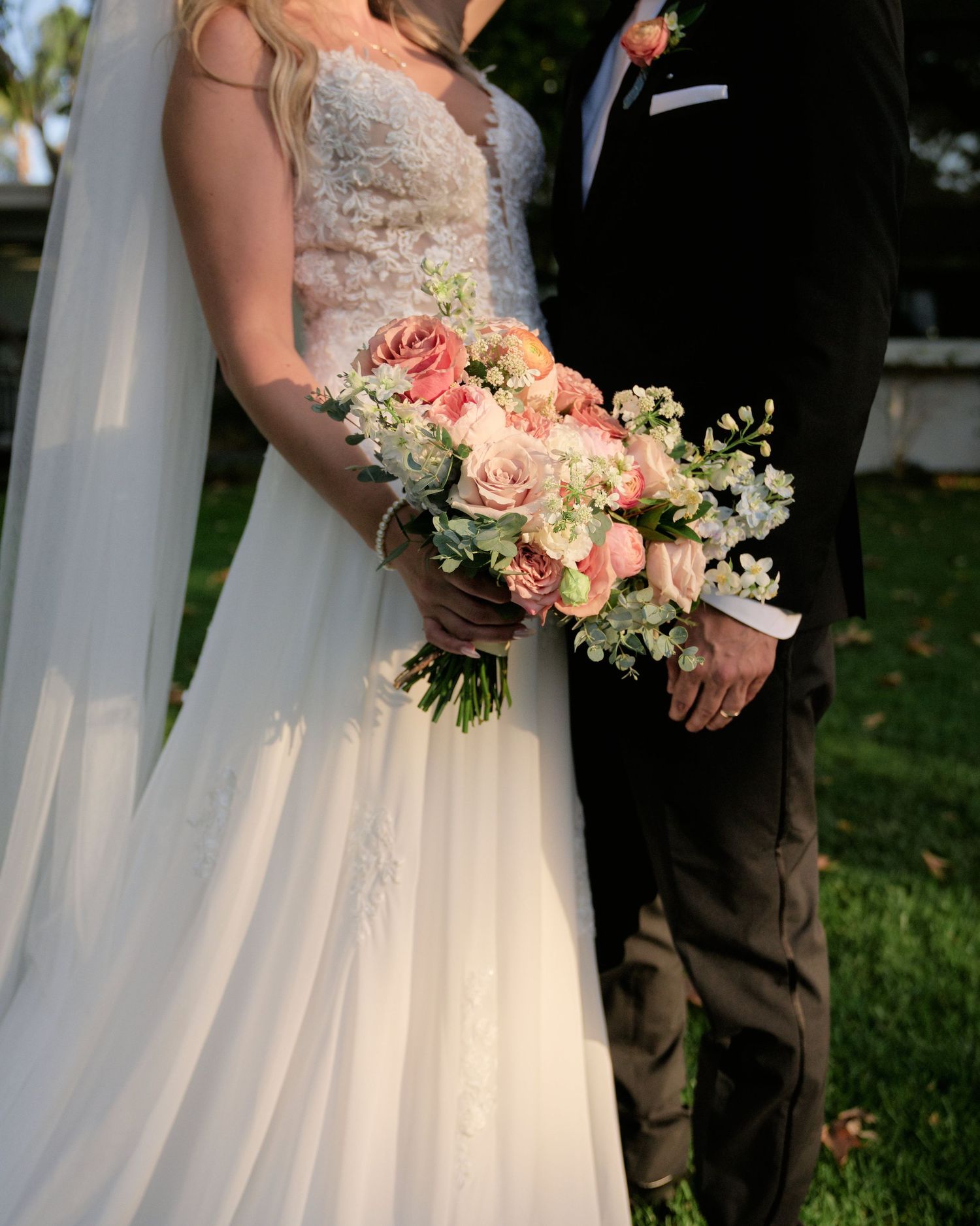An elegant wedding bouquet of pink and white flowers held between a bride and groom in formal attire.
