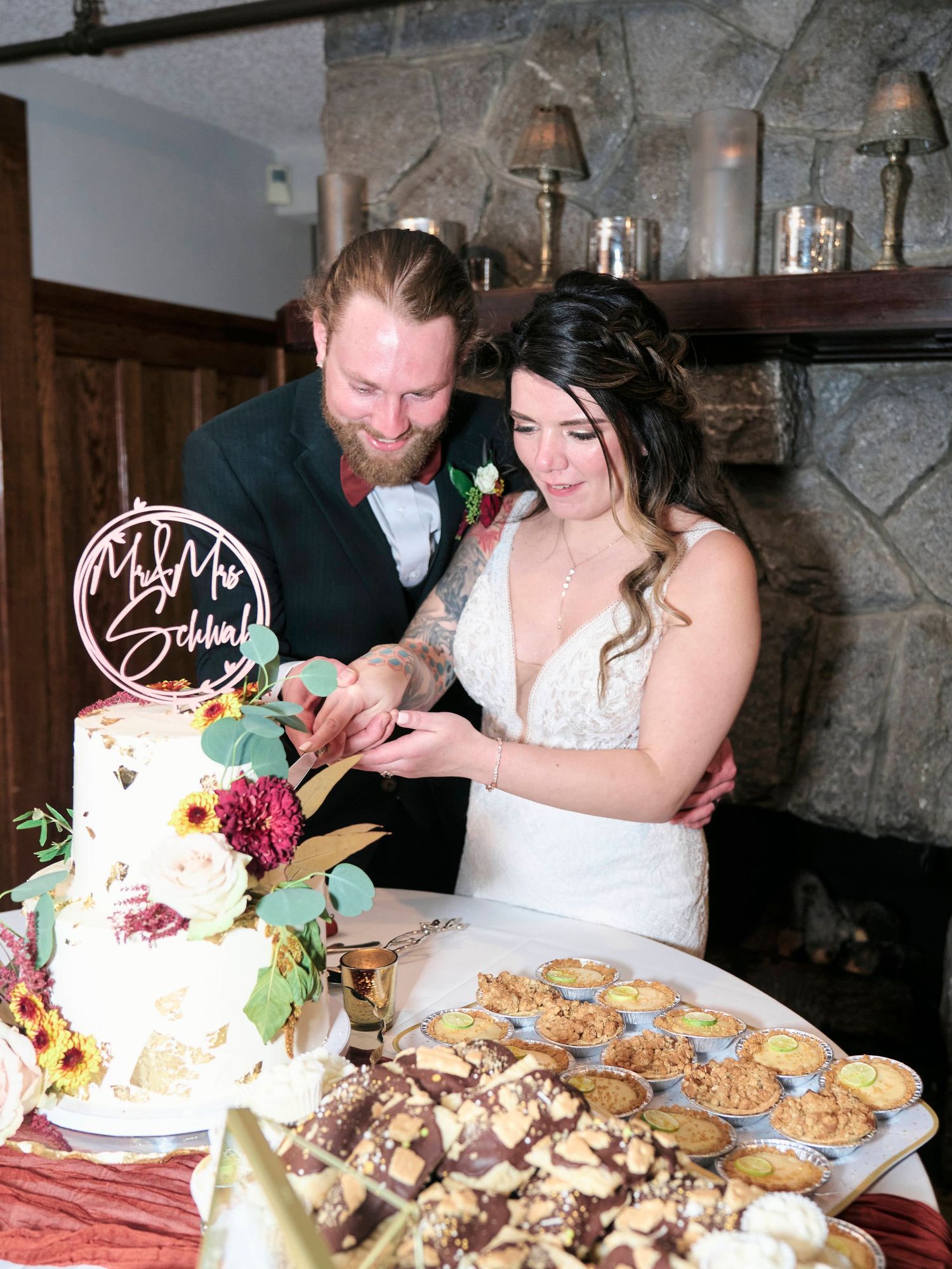Newlyweds cut their wedding cake decorated with greenery and florals at their reception.