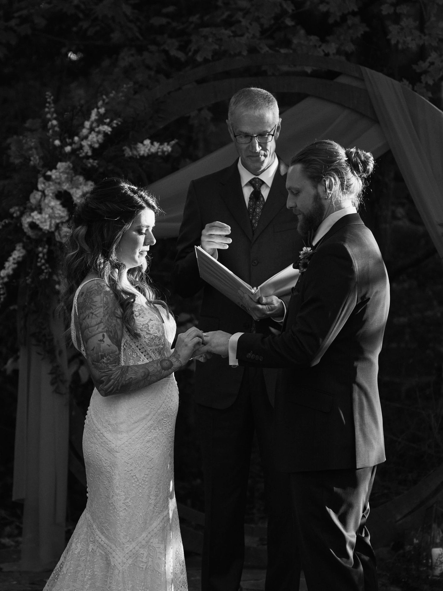 A black and white photo of a wedding ceremony under an arch with elegant floral decorations.