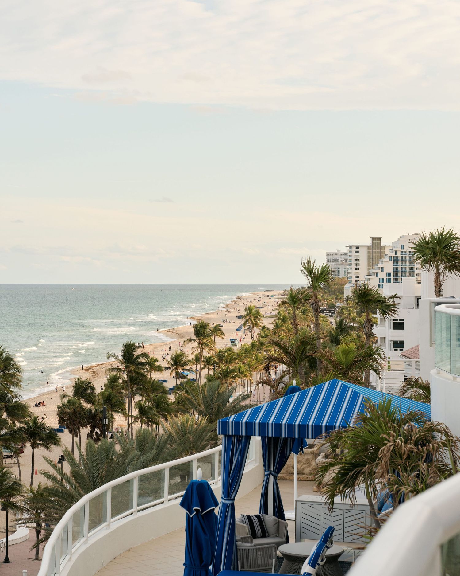 Coastal view of beach and palm trees with blue striped awning in foreground.