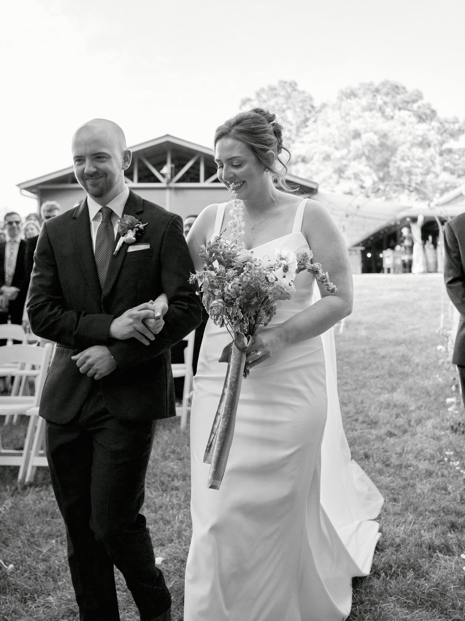 Black and white photo of couple walking together at outdoor ceremony venue.