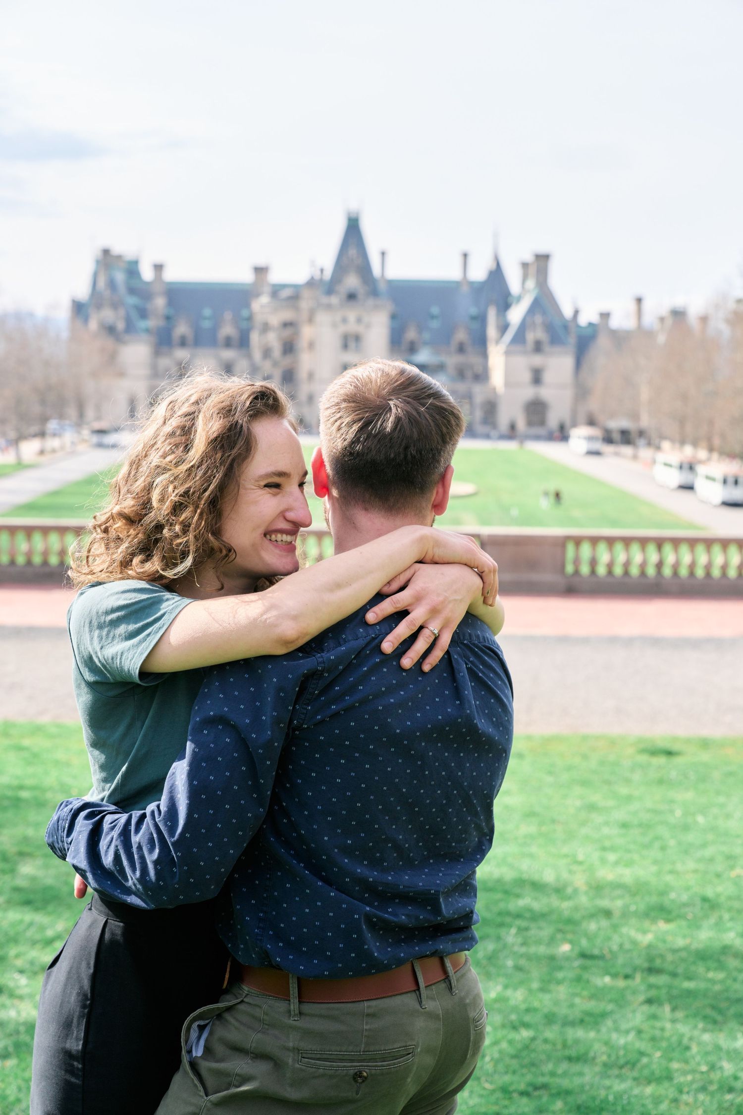 A couple embraces lovingly in front of the majestic Biltmore Estate surrounded by green lawns.