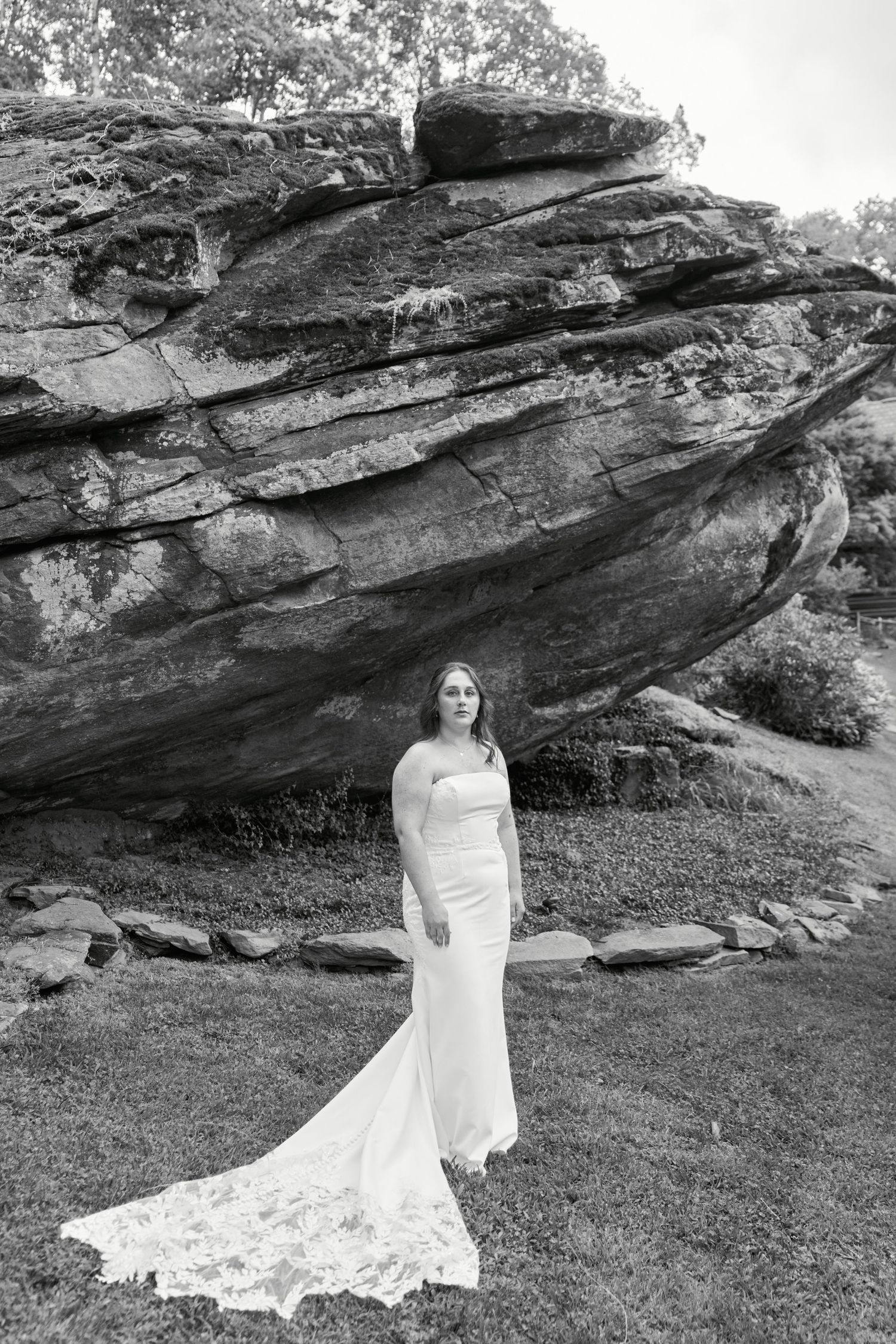 A black and white photograph of someone in a flowing white wedding dress standing in front of a dramatic rock formation.