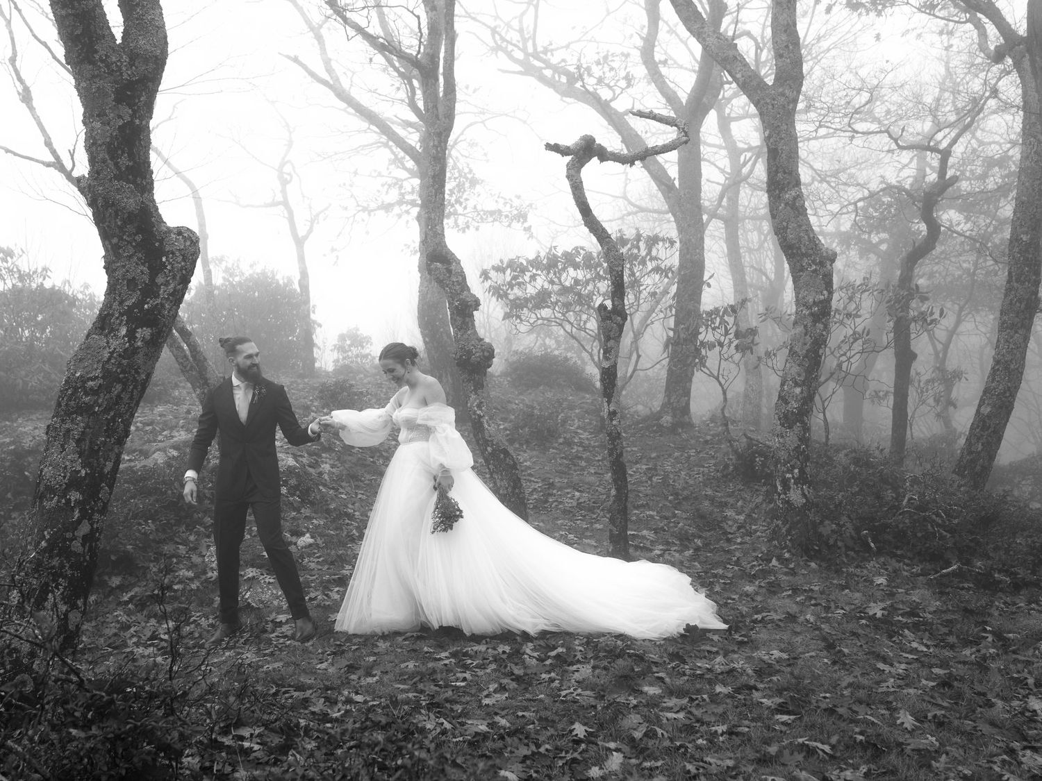 A black and white photo of newlyweds dancing in a mystical foggy forest.