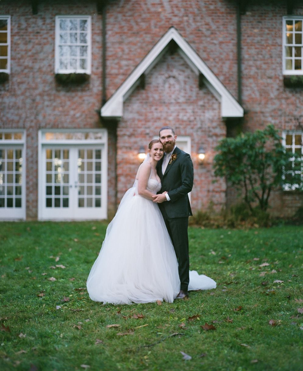A romantic wedding portrait of a couple standing before a charming brick country house.
