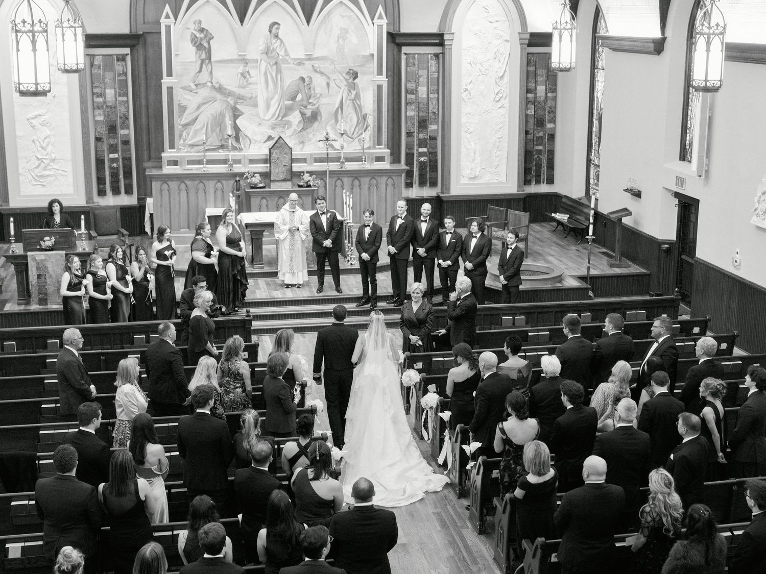 Black and white photo of an elegant church wedding ceremony with bride, groom, and wedding party at the altar.
