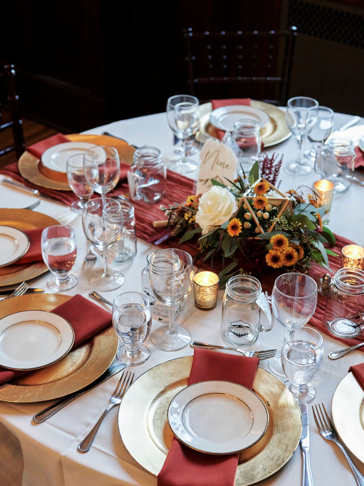 Elegant table setting with gold chargers, burgundy napkins, and floral centerpiece for a formal dinner event.