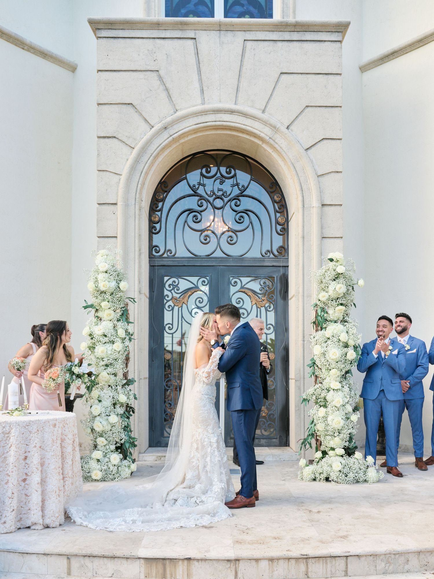 Couple shares first kiss as married couple in front of decorated church entrance.
