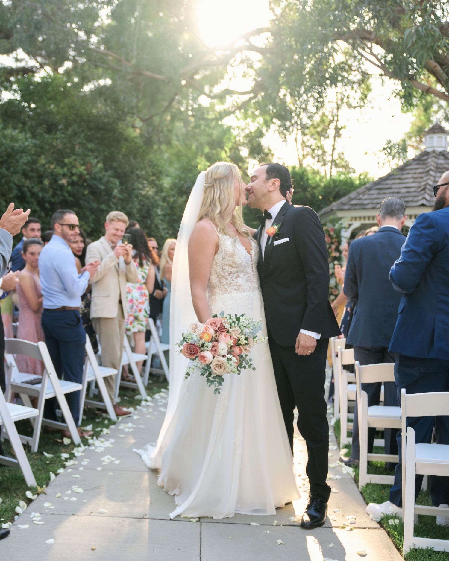 Wedding couple shares a romantic moment on a garden path lined with white chairs.
