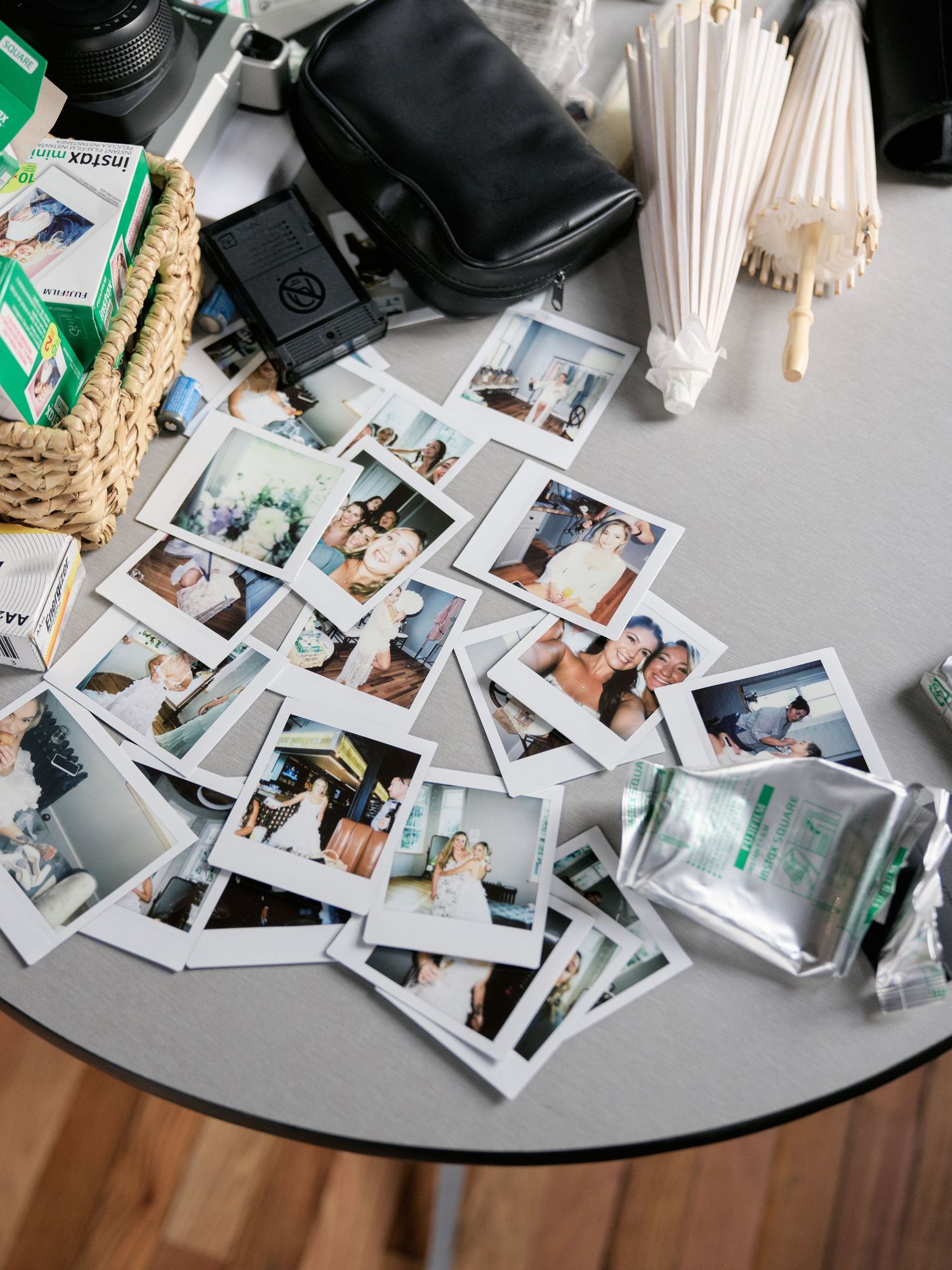 A collection of polaroid instant photos scattered on a gray table alongside a black bag and white paper straws.
